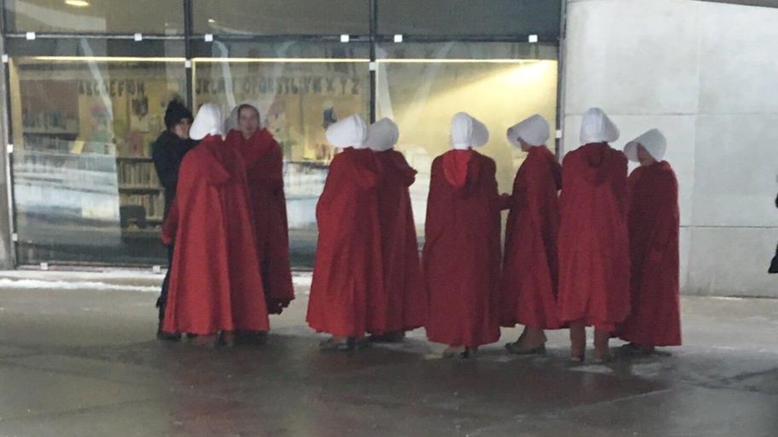 Un groupe d'actrices vêtues de robes rouges et de chapeaux blancs devant un édifice.