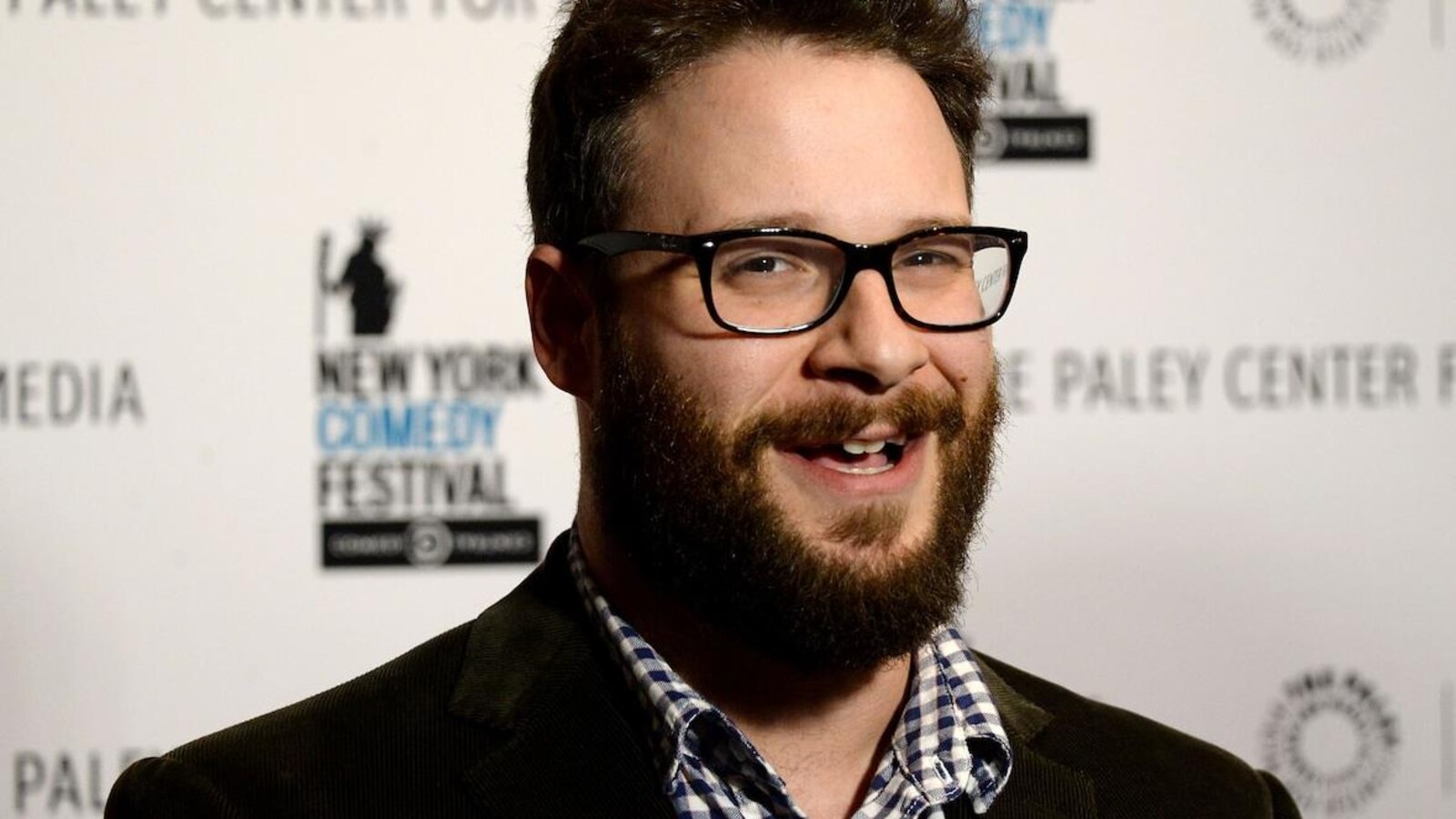 Seth Rogen sourit pour la caméra devant une affiche du New York Comedy Festival.