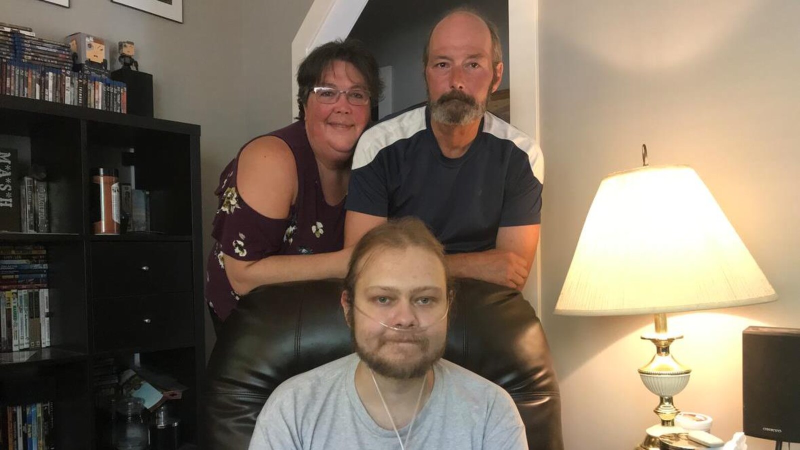 Un jeune homme malade assis dans son salon et entouré par ses parents.