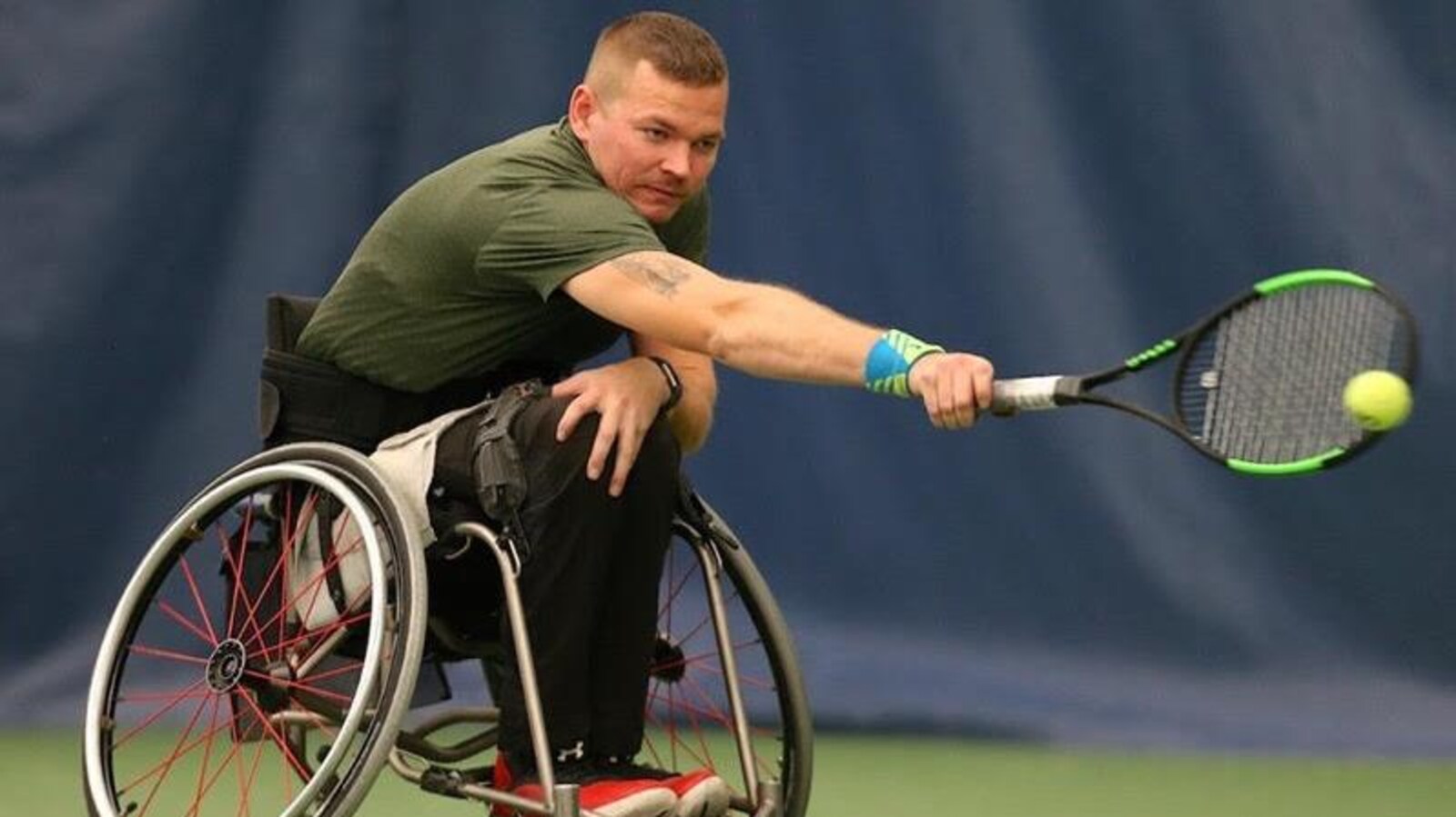 Un homme est assis dans un fauteuil roulant. Il joue au tennis.