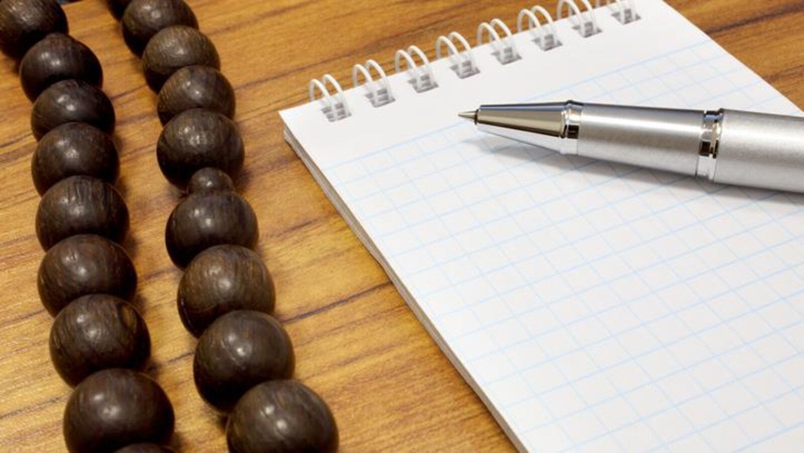 Un collier religieux sur un bureau, près d'un carnet de note et d'un stylo.