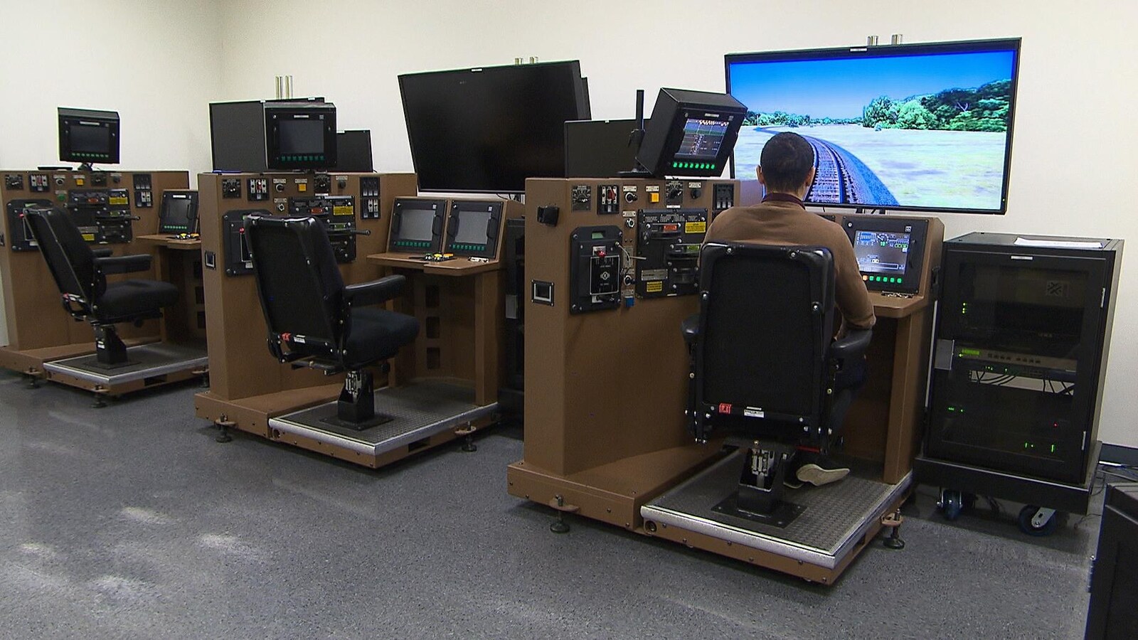Un homme devant une console et un écran qui simulent la conduite d'une locomotive