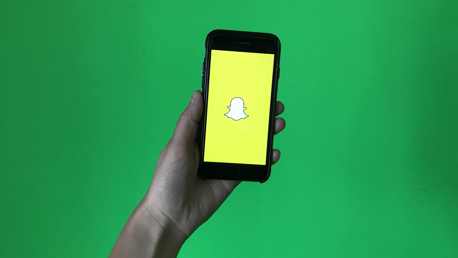 Un téléphone mobile avec le logo de Snapchat tenu dans une main devant un tableau vert