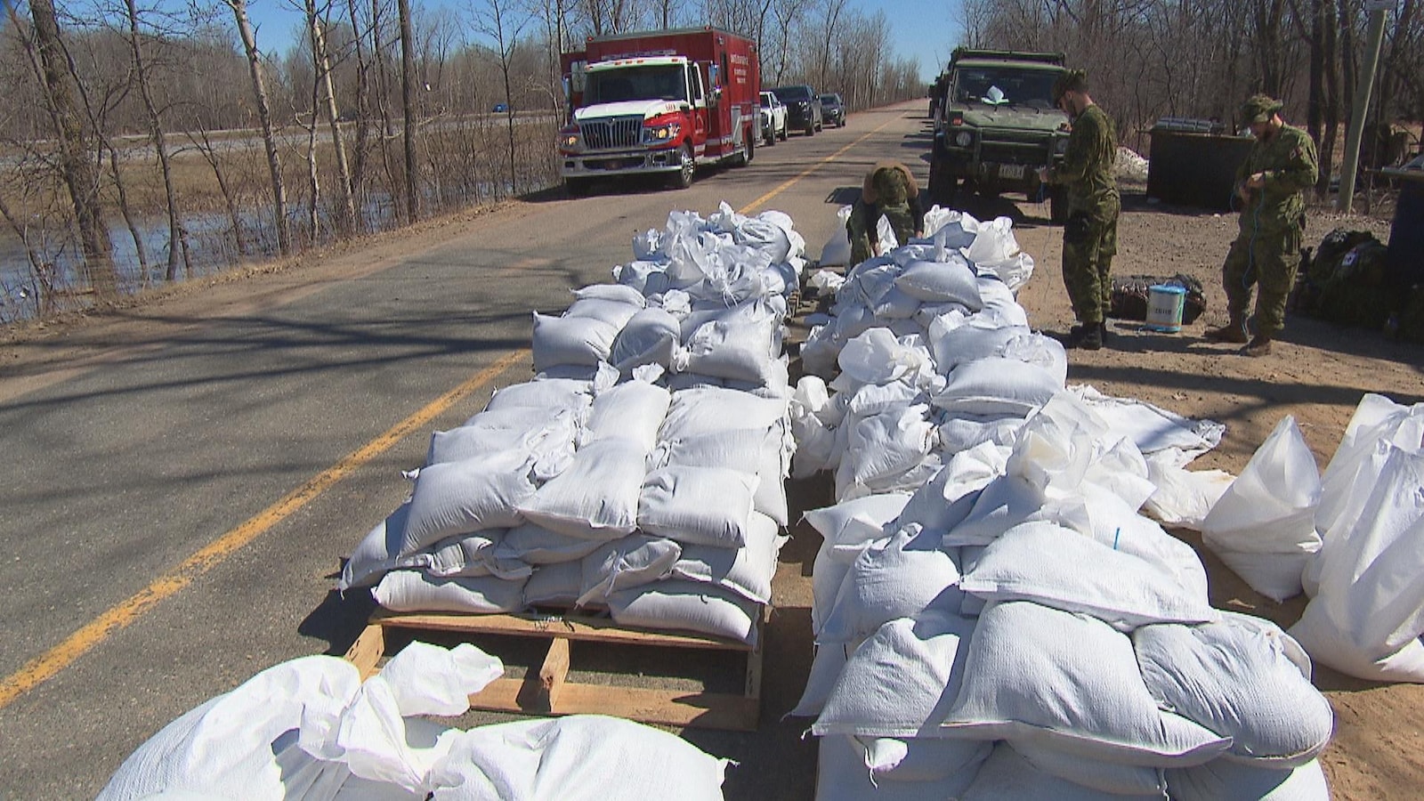 Des soldats travaillent près de palettes de sacs de sable en bordure de route.