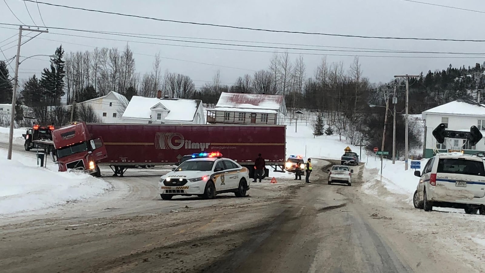 La remorque d'un camion de livraison bloque une route. Des voitures de police l'entourent.