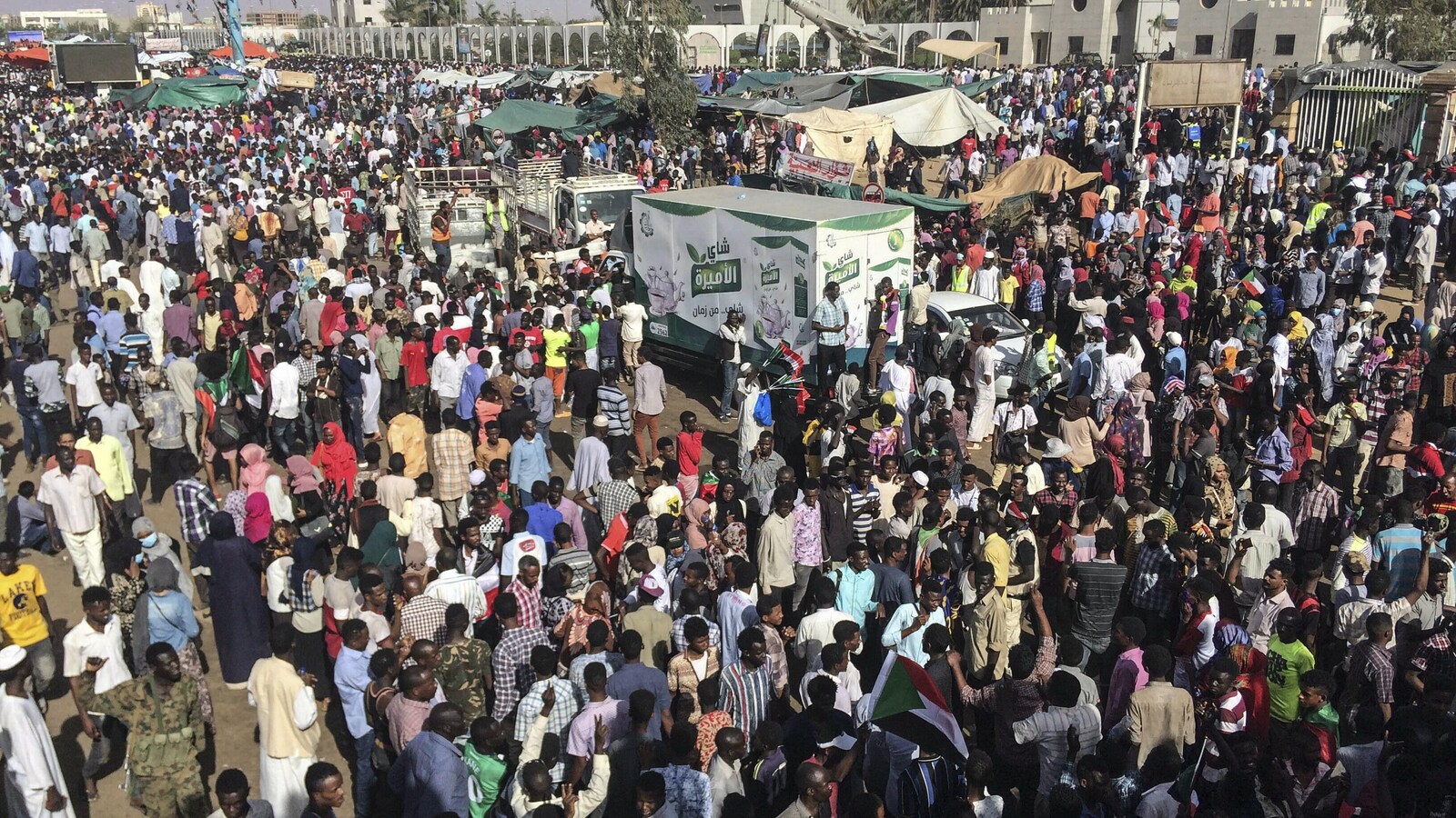 Plusieurs milliers de personnes sont rassemblées avec des tentes et des camions de nourriture près d'un bâtiment administratif.