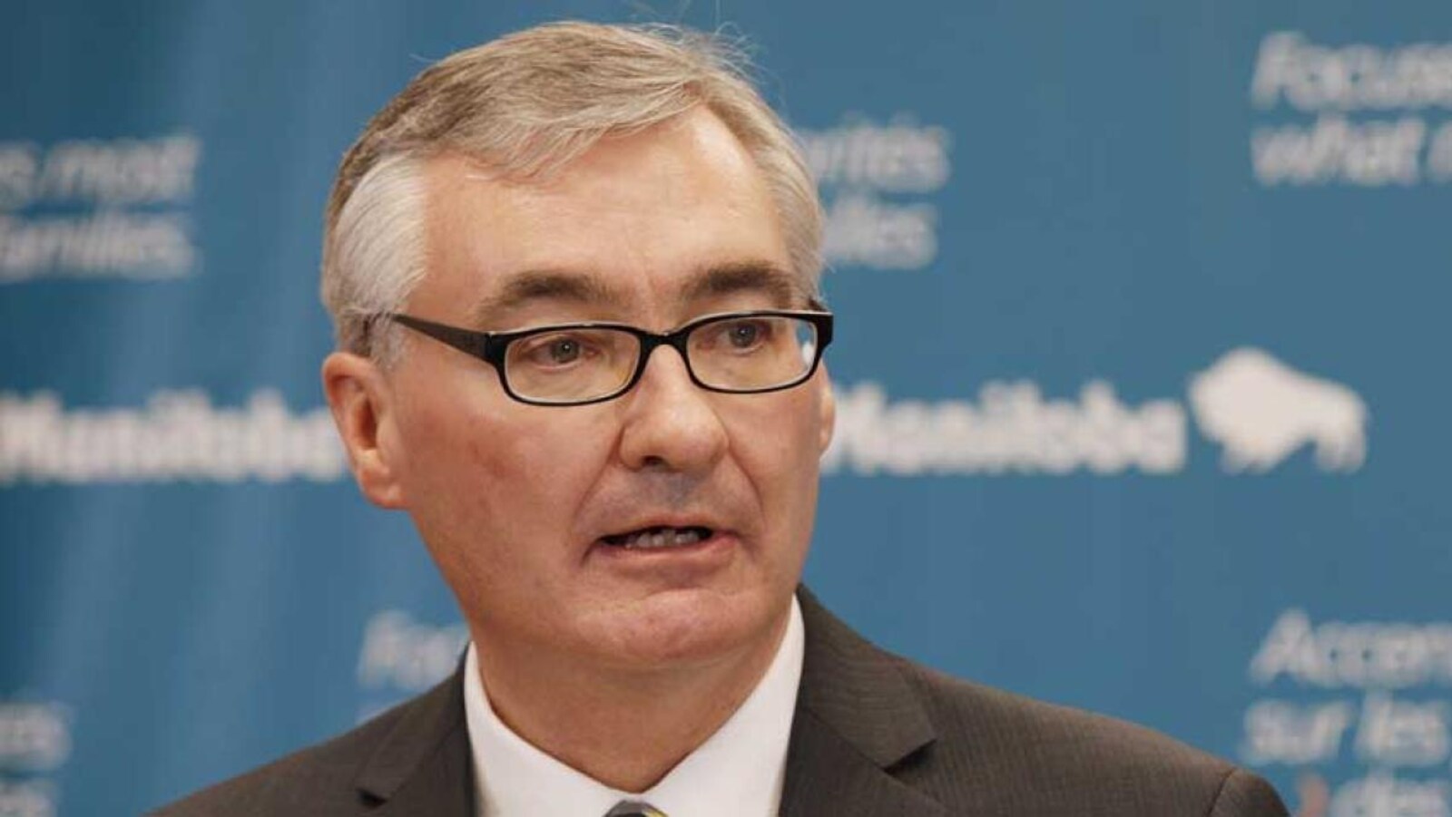 Un homme portant des lunettes et ayant des cheveux grisonnants, vu en gros plan.