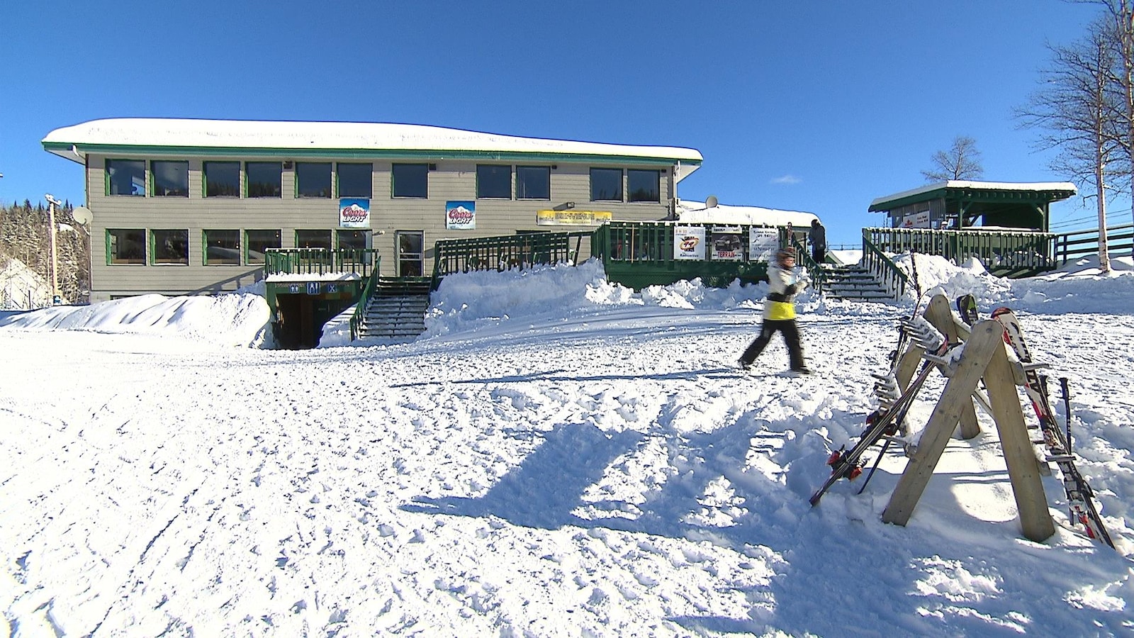 Le chalet avec une personne qui va chercher ses skis en avant-plan