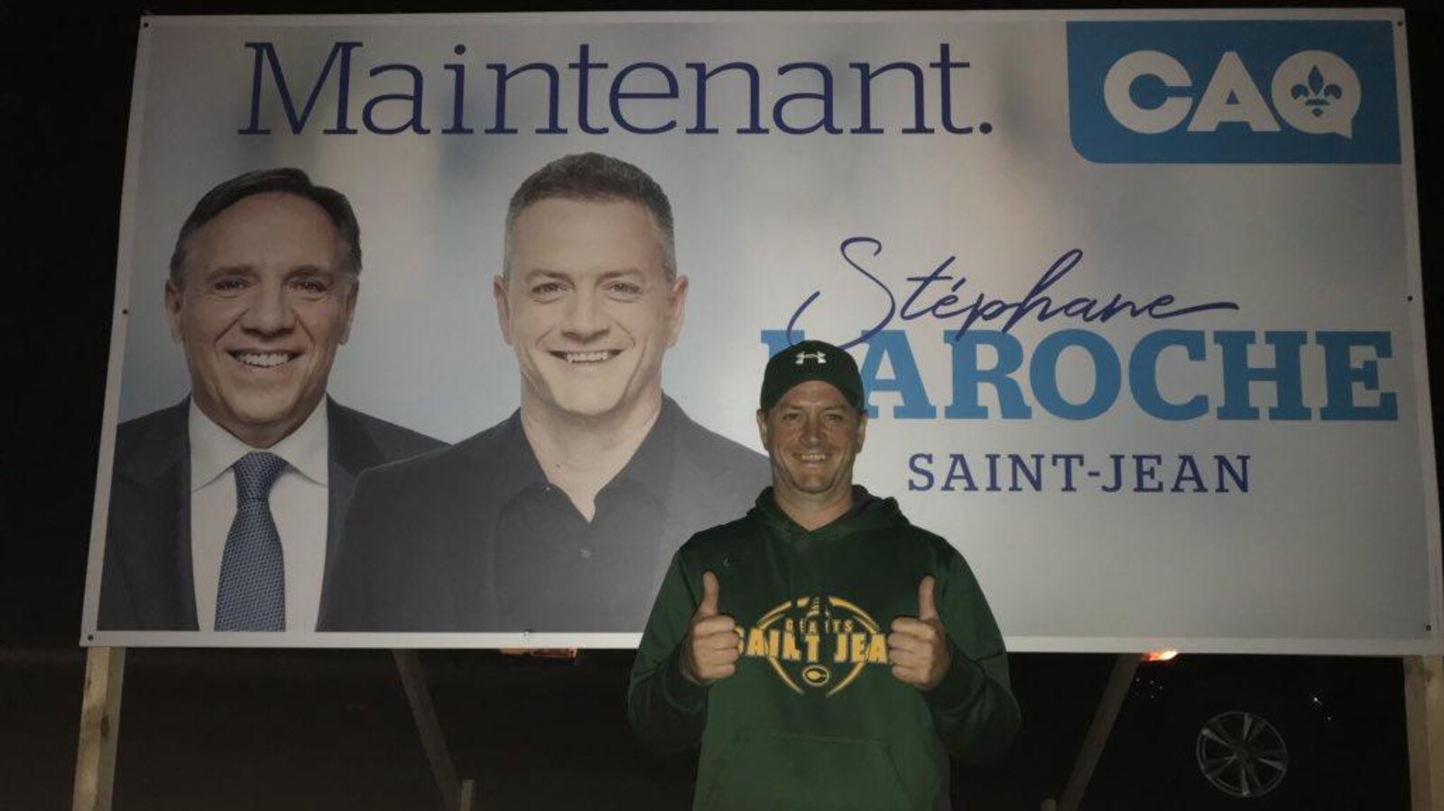Stéphane Laroche pose devant une pancarte électorale le montrant aux côtés de François Legault.