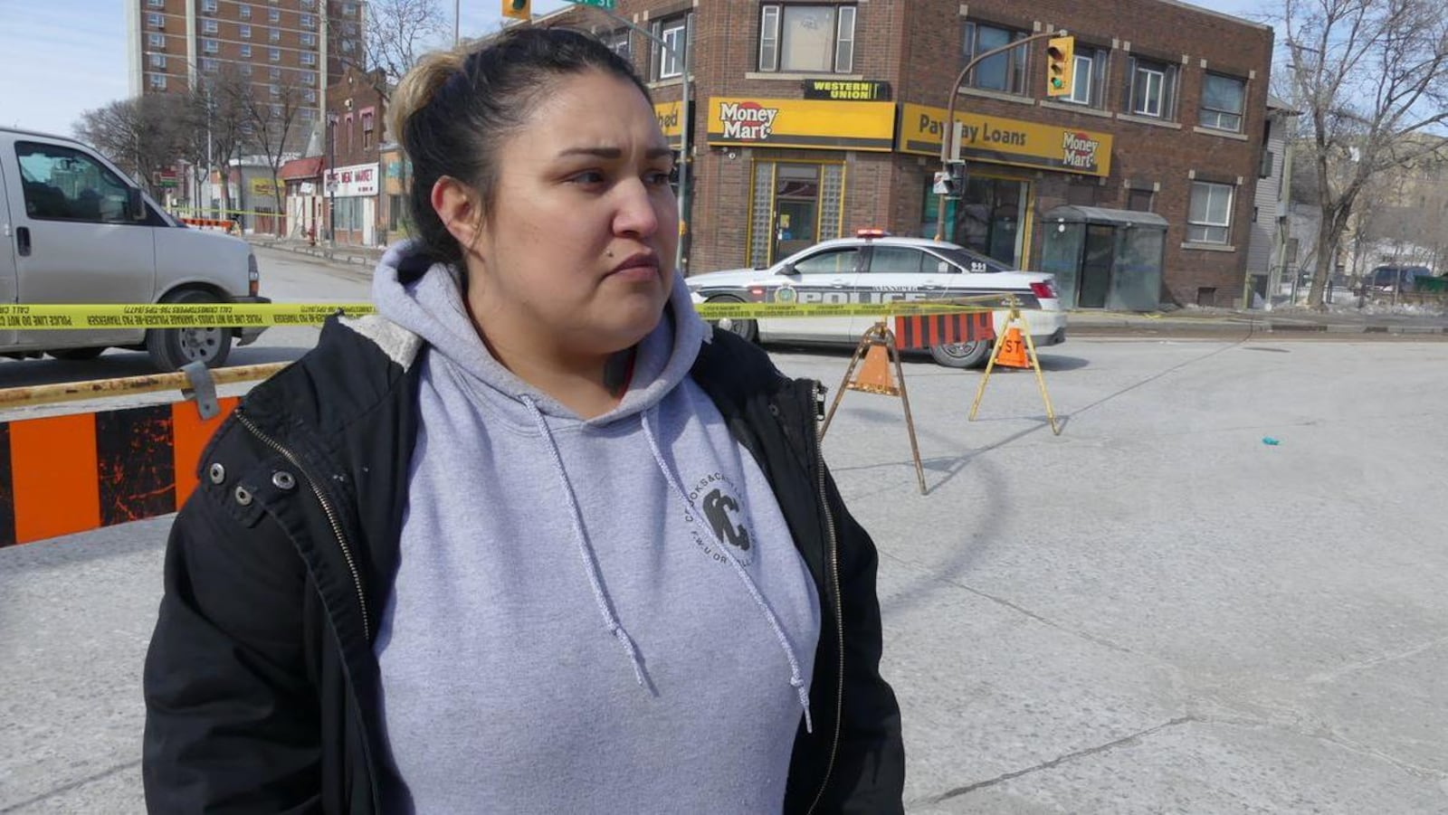 Une femme debout devant le ruban jaune d'un cordon policier et des auto-patrouilles.