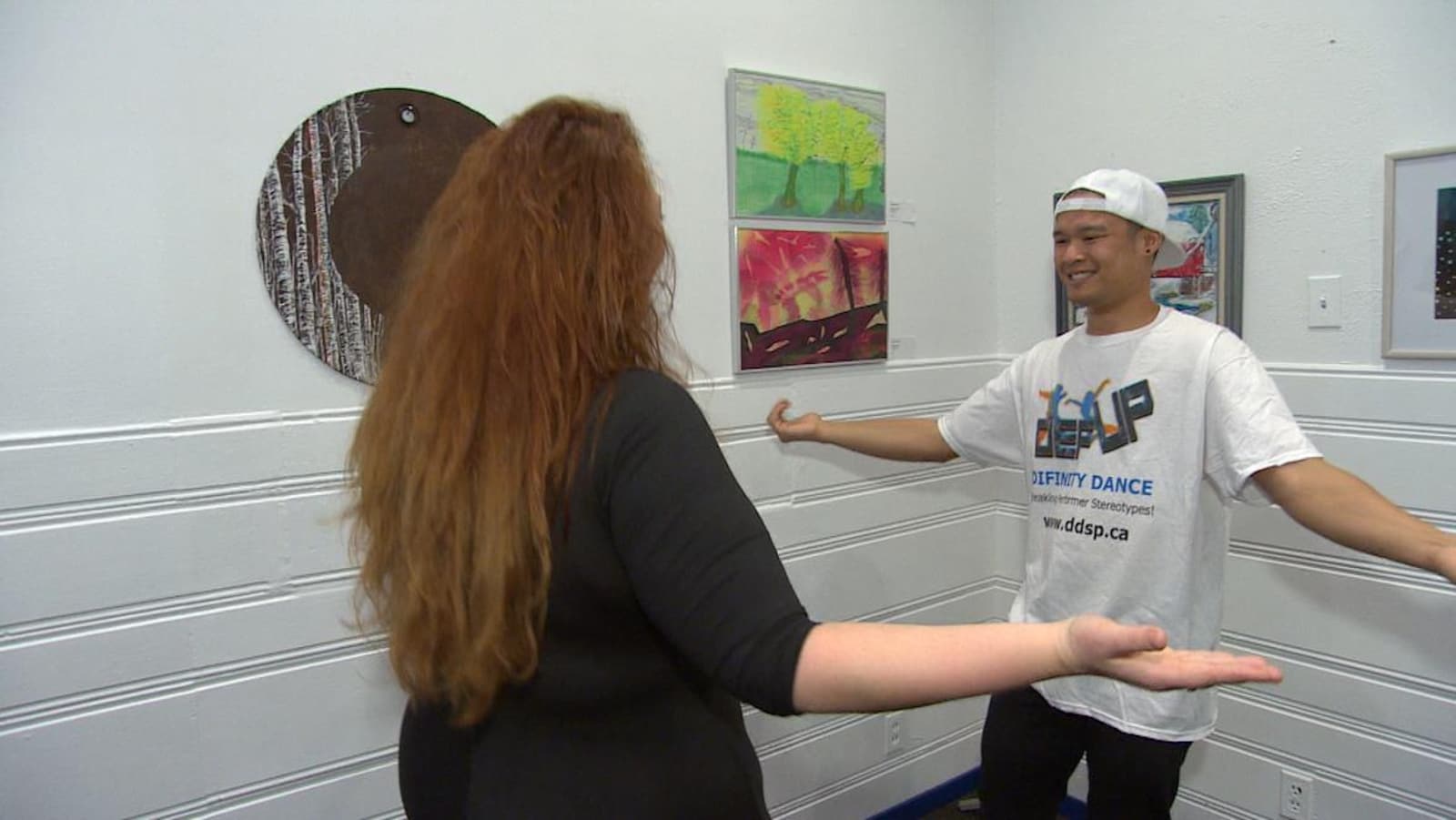 Stephanie Strugar (à gauche) et Jordan Sangalang (à droite) pratiquent des mouvements de danse dans une salle aux murs décorés de toiles peintes.