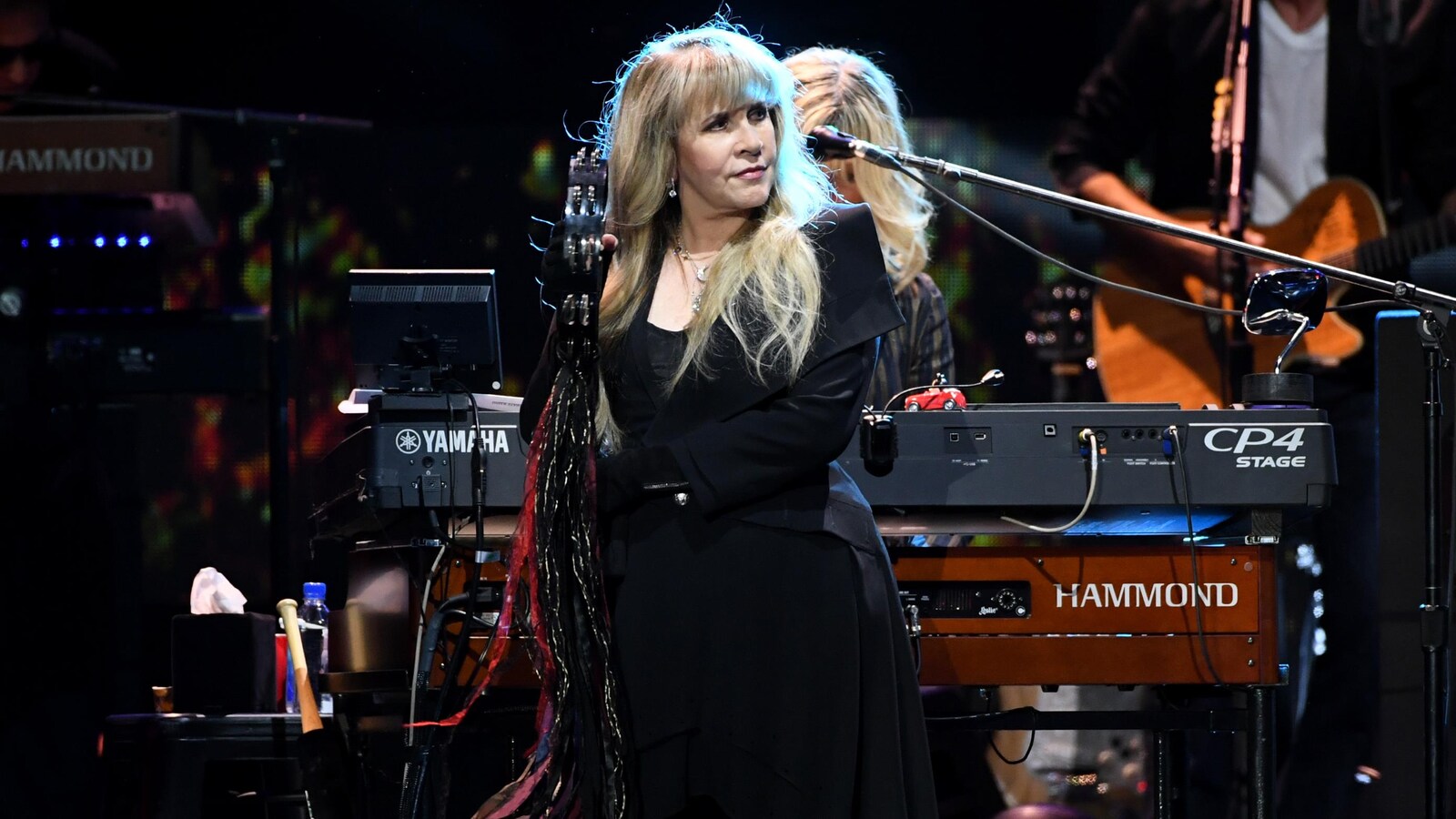 Stevie Nicks debout sur scène face au public, deux musiciens derrière elle.