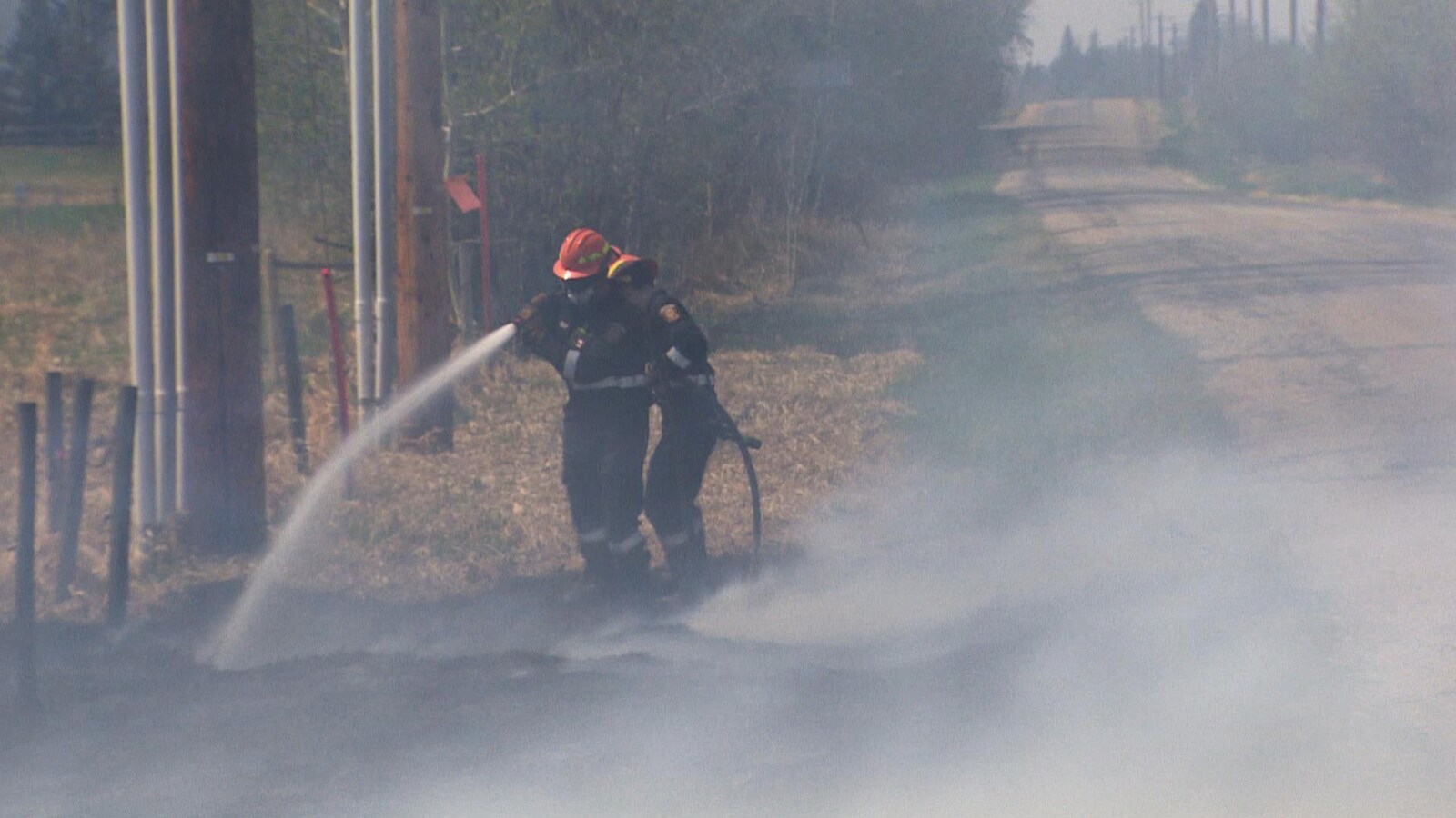 Des pompiers tiennent une lance d'incendie sur la route 564.