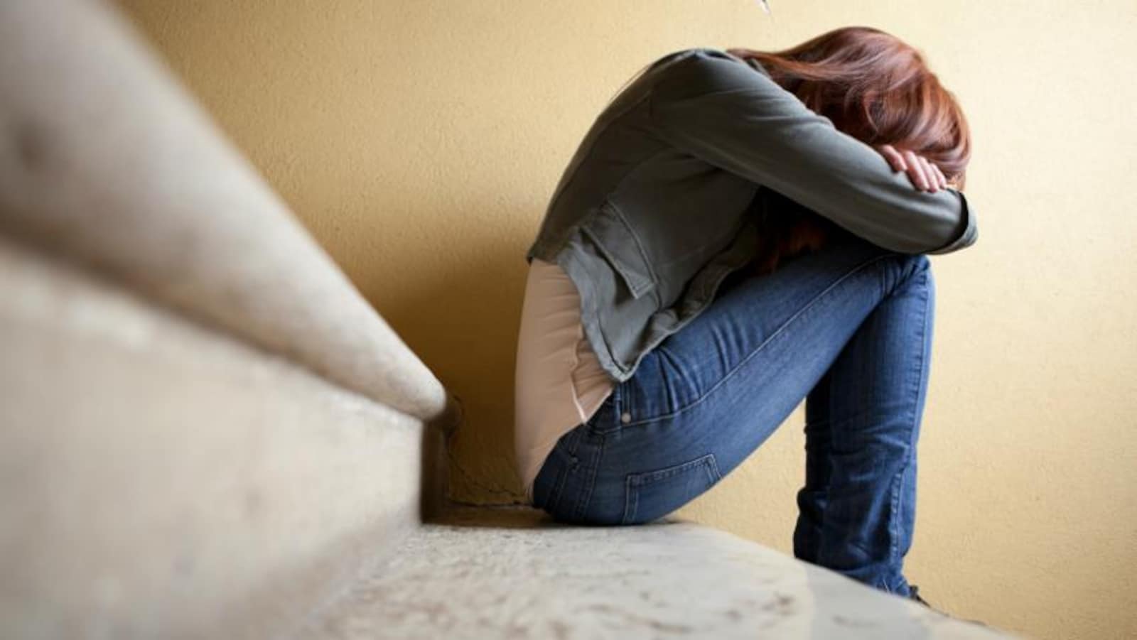 Une jeune femme assise dans les marches d'un escalier, recroquevillée sur elle-même