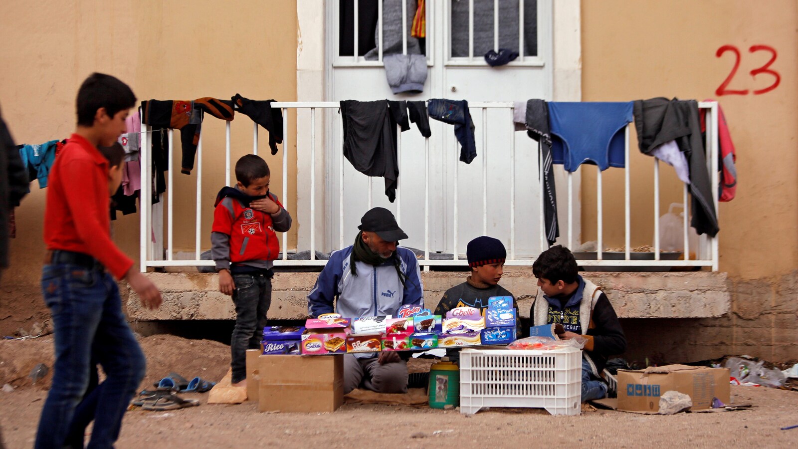 Un homme entouré d'enfants sont assis sur le sol dans un camp de déplacés non loin de Damas en train de vendre des friandises.