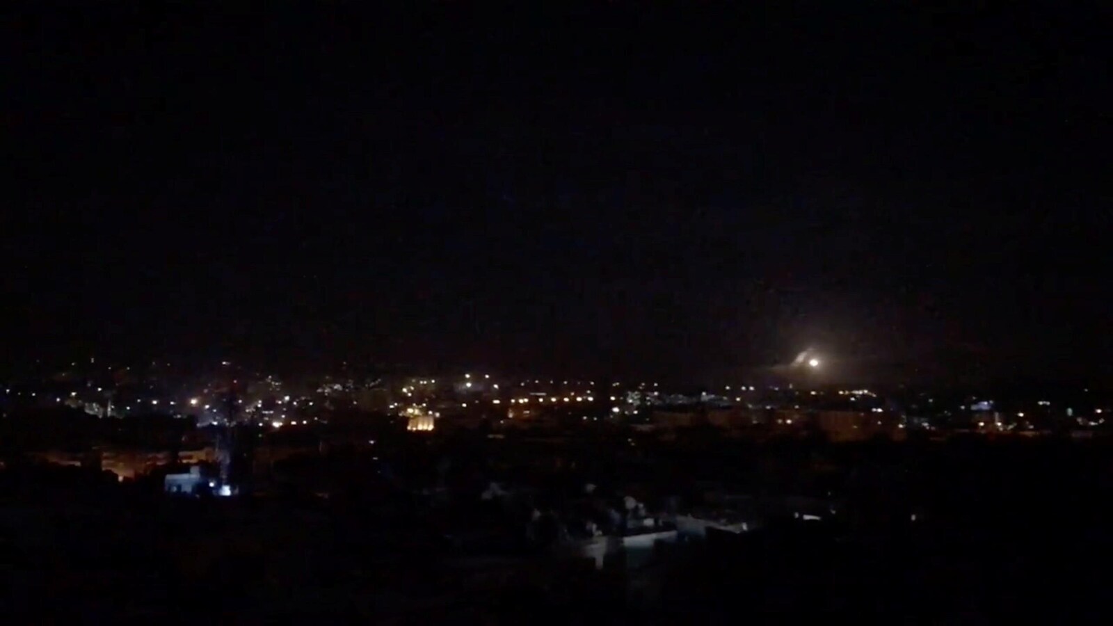 Une photo tirée d'une vidéo montre un point lumineux au loin dans la nuit sur une ville syrienne.
