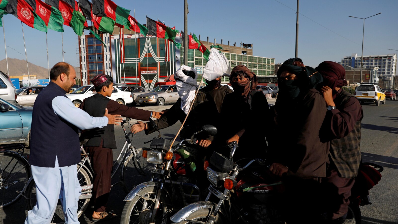 Des talibans sur des motocyclettes, le visage voilé, serrent la main de deux résidents de Kaboul.