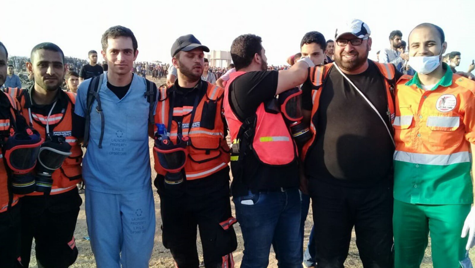 Photo d'un homme en tenue de médecin bleue et de six autres hommes portant des dossards oranges.