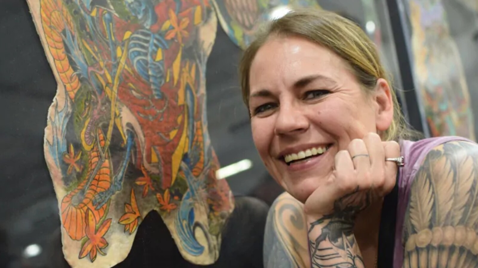 Cheryl Wenzel pose avec le sourire devant les tatouages de son mari décédé.