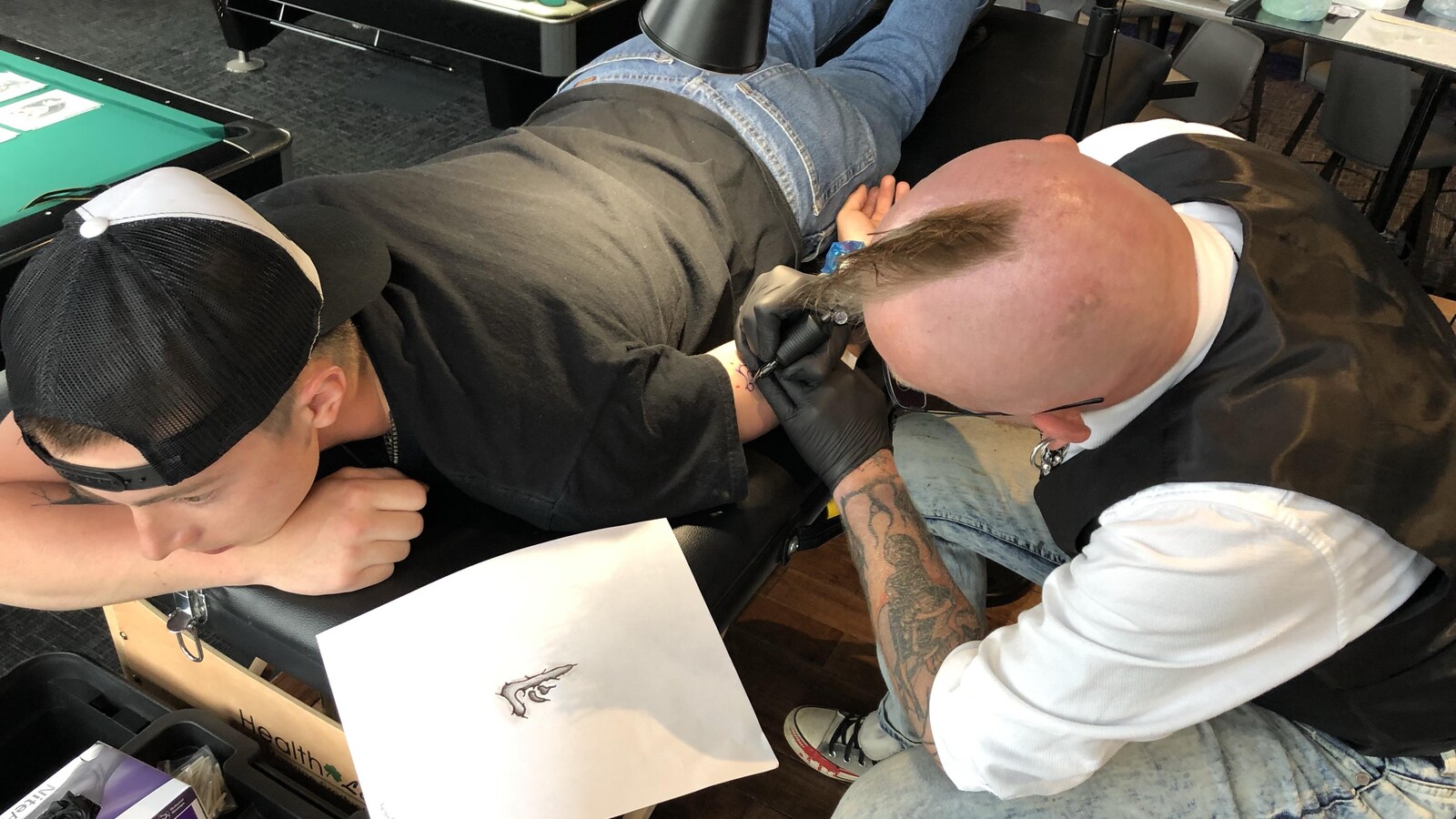 Un tatoueur dessine un symbole abstrait sur le bras d'un client.