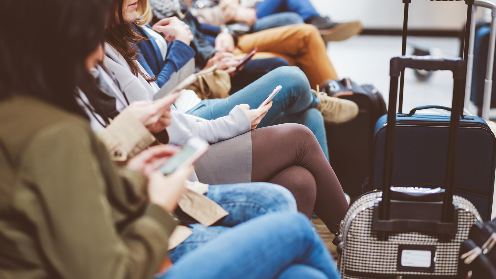 Des voyageurs patientent à l'aéroport en consultant leur téléphone intelligent.