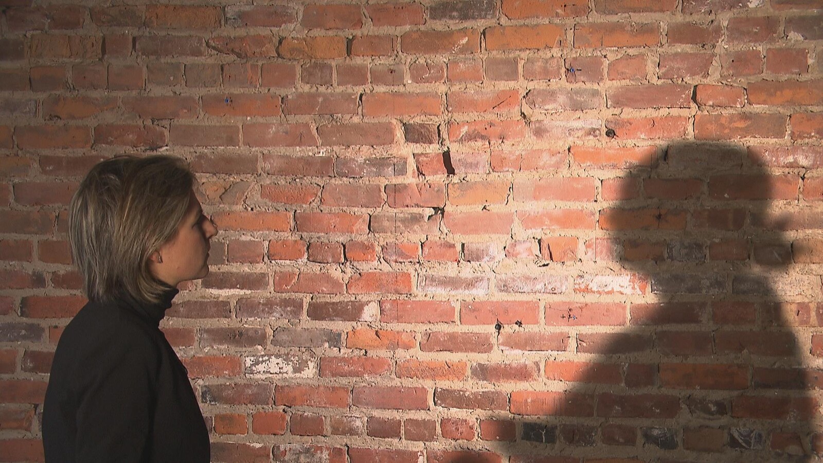 Ombre d'une personne sur un mur de brique en entrevue avec une femme qui porte un chandail noir.