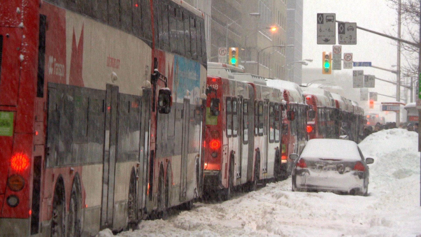 Plusieurs autobus arrêtés à un feu de circulation, sous la neige.
