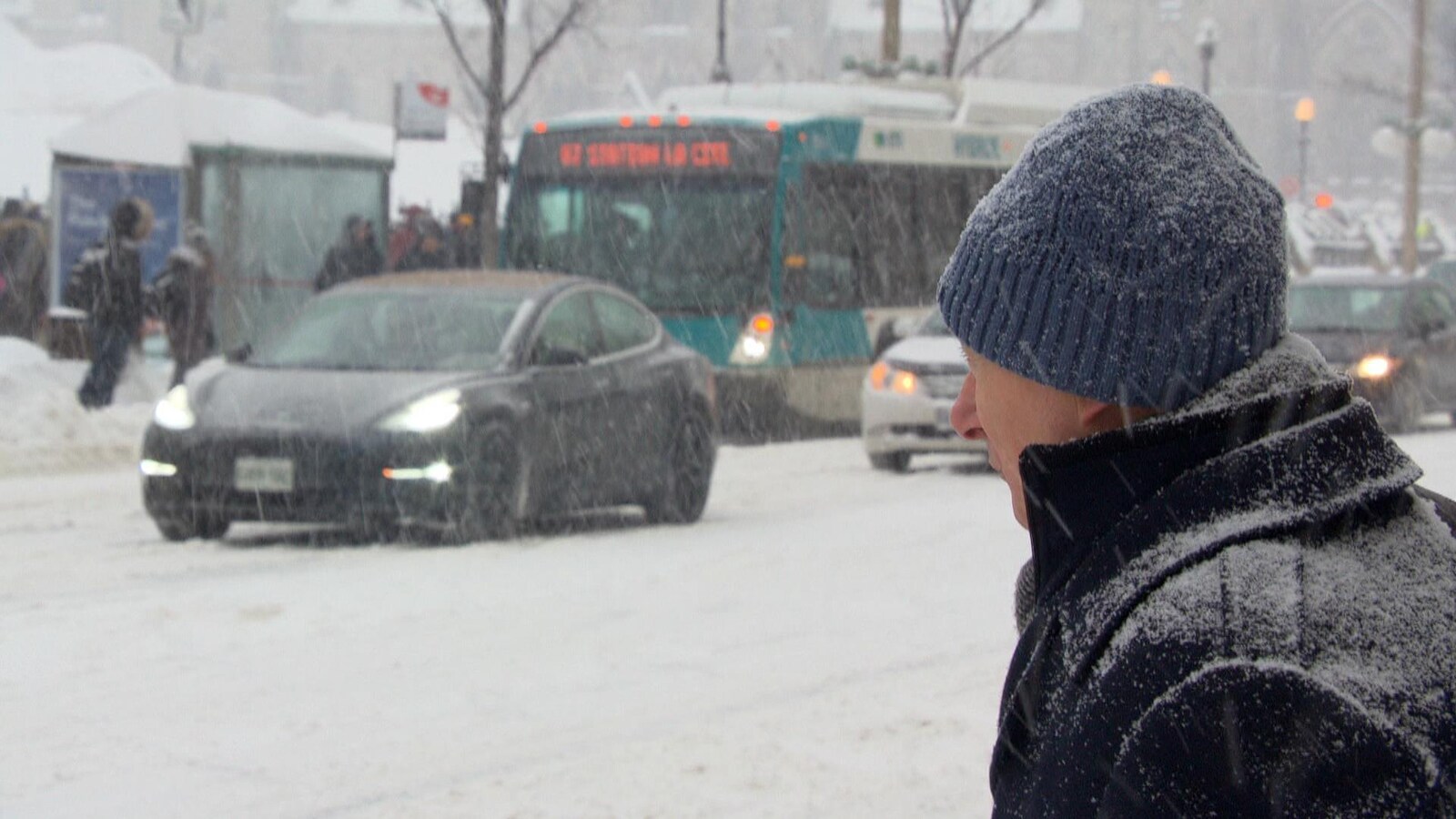 Un homme attend pour traverser la rue sous la neige.