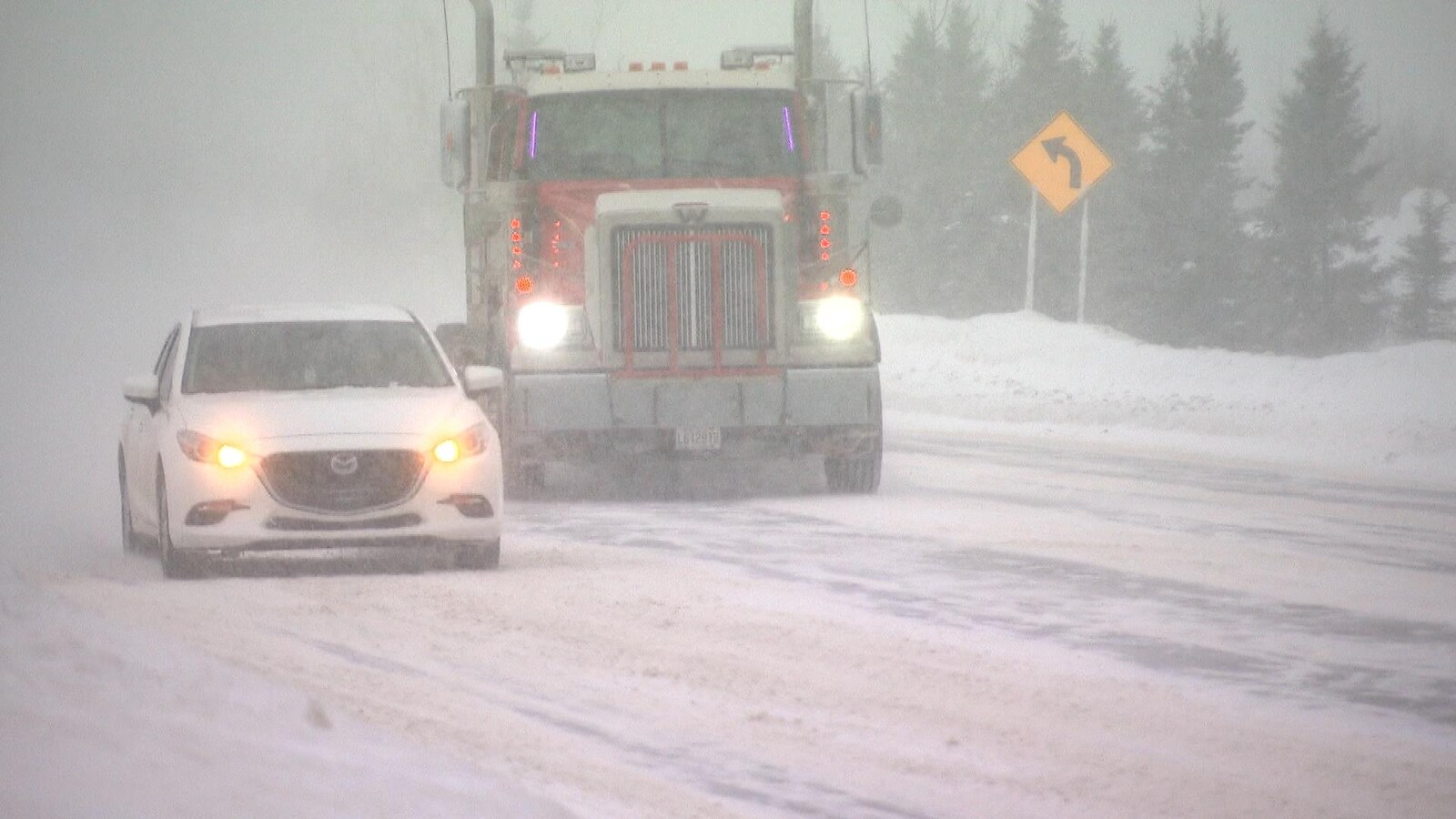 Un camion et un véhicule circulent sur une route enneigée.