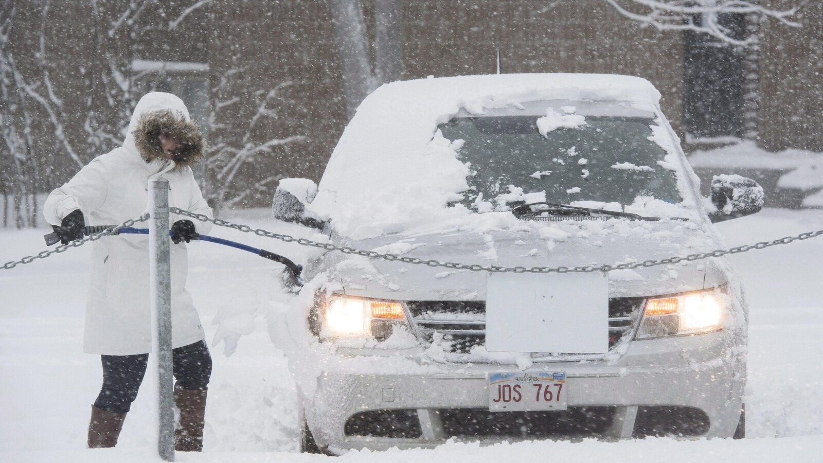 Une femme déneige sa voiture pendant une tempête de neige.