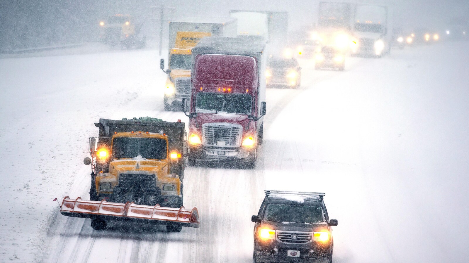 Plusieurs véhicules circulent sur une route enneigée alors que de nombreux flocons de neige tombent toujours du ciel.
