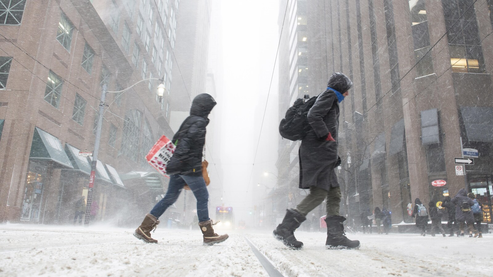 Des piétons traversent une rue du centre-ville de Toronto pendant une tempête de neige.
