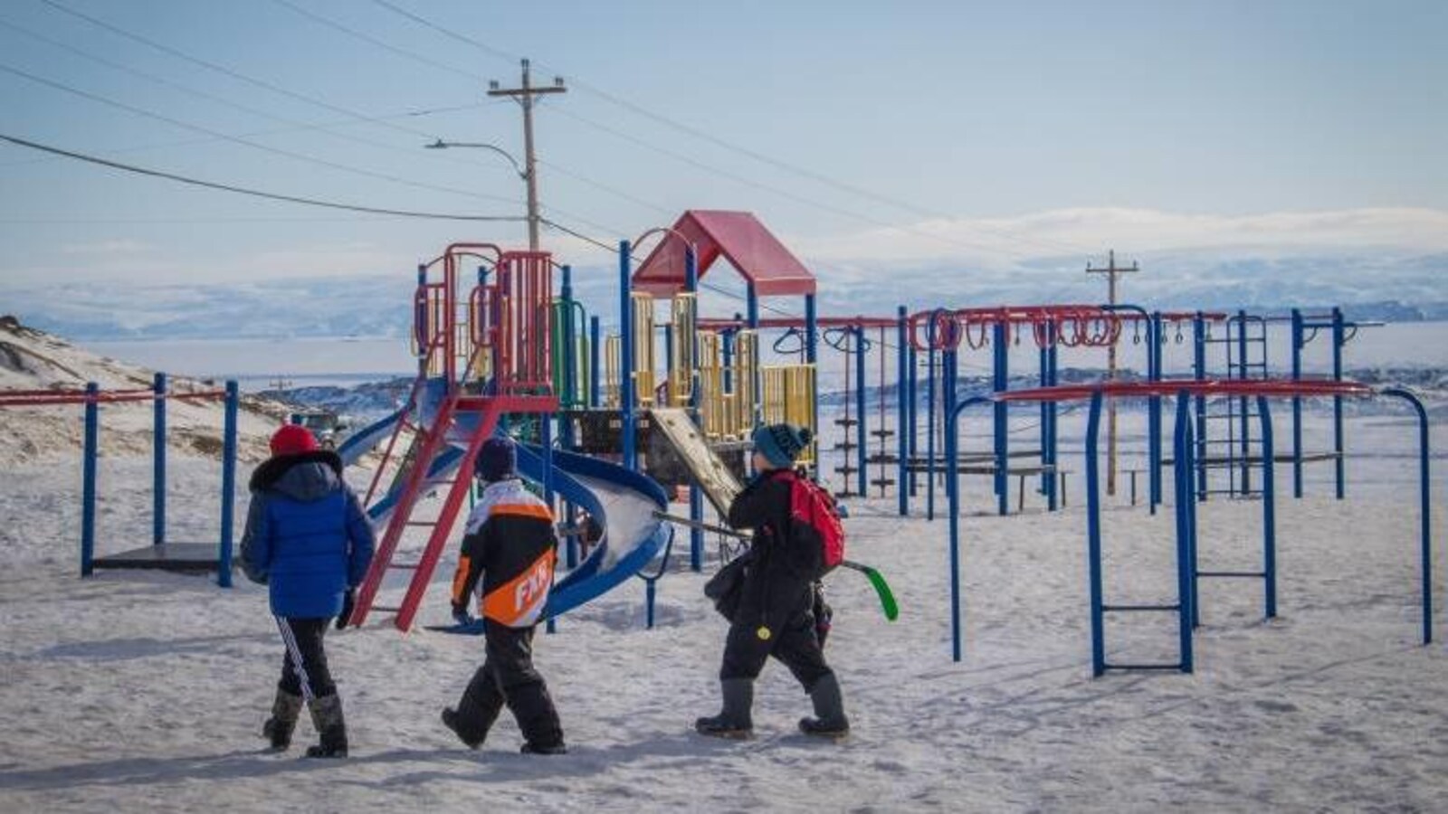 Des enfants vêtus chaudement traversent un terrain de jeu devant un paysage montagneux.