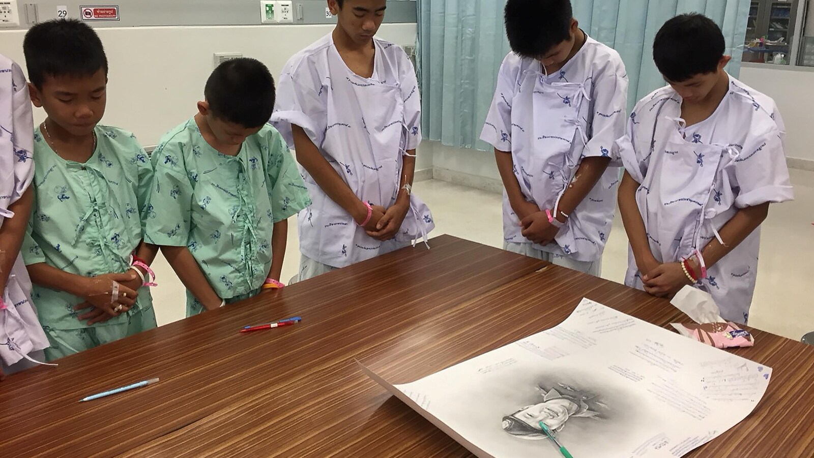 De jeunes rescapés observant une minute de silence autour d'un portrait de l'ancien plongeur de la marine thaïlandaise Saman Kunan qui a péri le 6 juillet alors qu'il tentait de les sauver de la grotte.