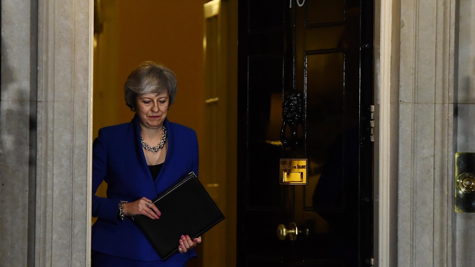 Theresa May, regardant au sol et tenant un porte-document, sort par l'entrée principale du 10 Downing Street, à Londres.