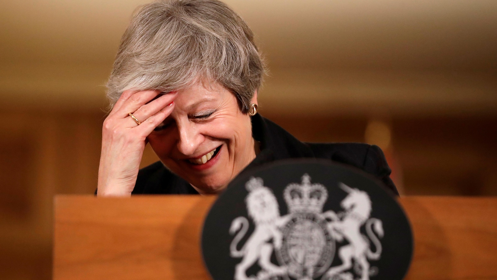 Theresa May rit et se touche le front de la main pendant une conférence de presse.