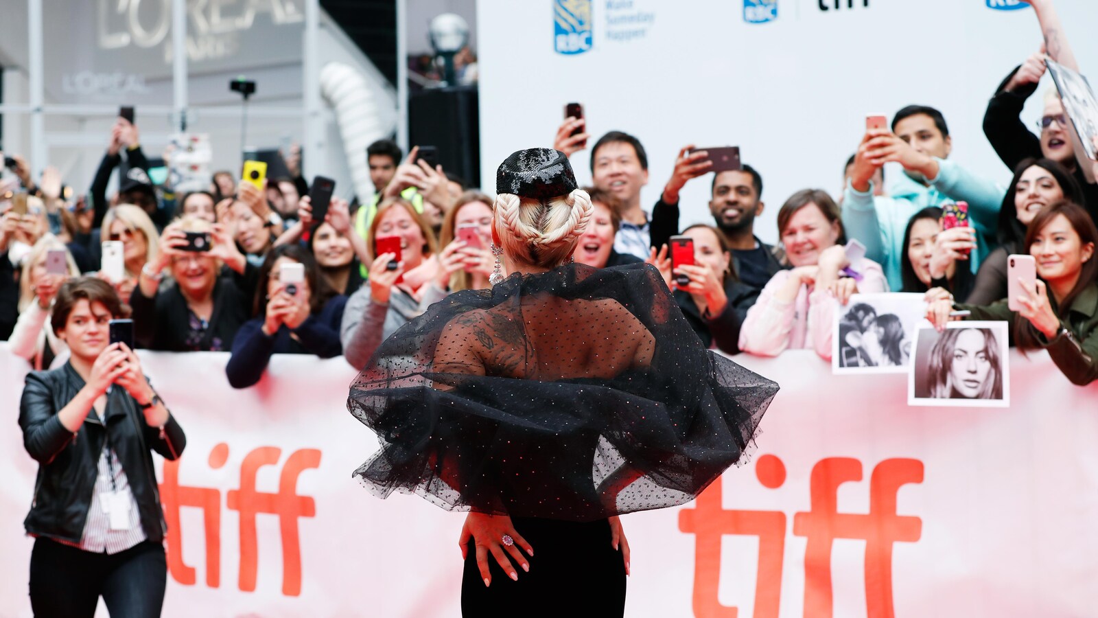 La chanteuse et actrice Lady Gaga à son arrivée sur le tapis rouge de la première du film <em>A Star is Born</em>, au Festival international du film de Toronto. De nombreuses personnes prennent des photos avec leurs téléphones intelligents derrière une barrière portant le logo du festival.
