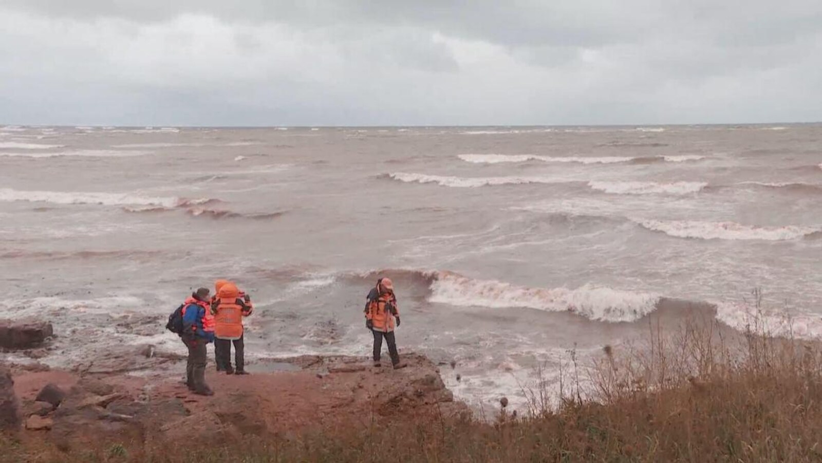 Trois personnes sur la côte regardent vers la mer