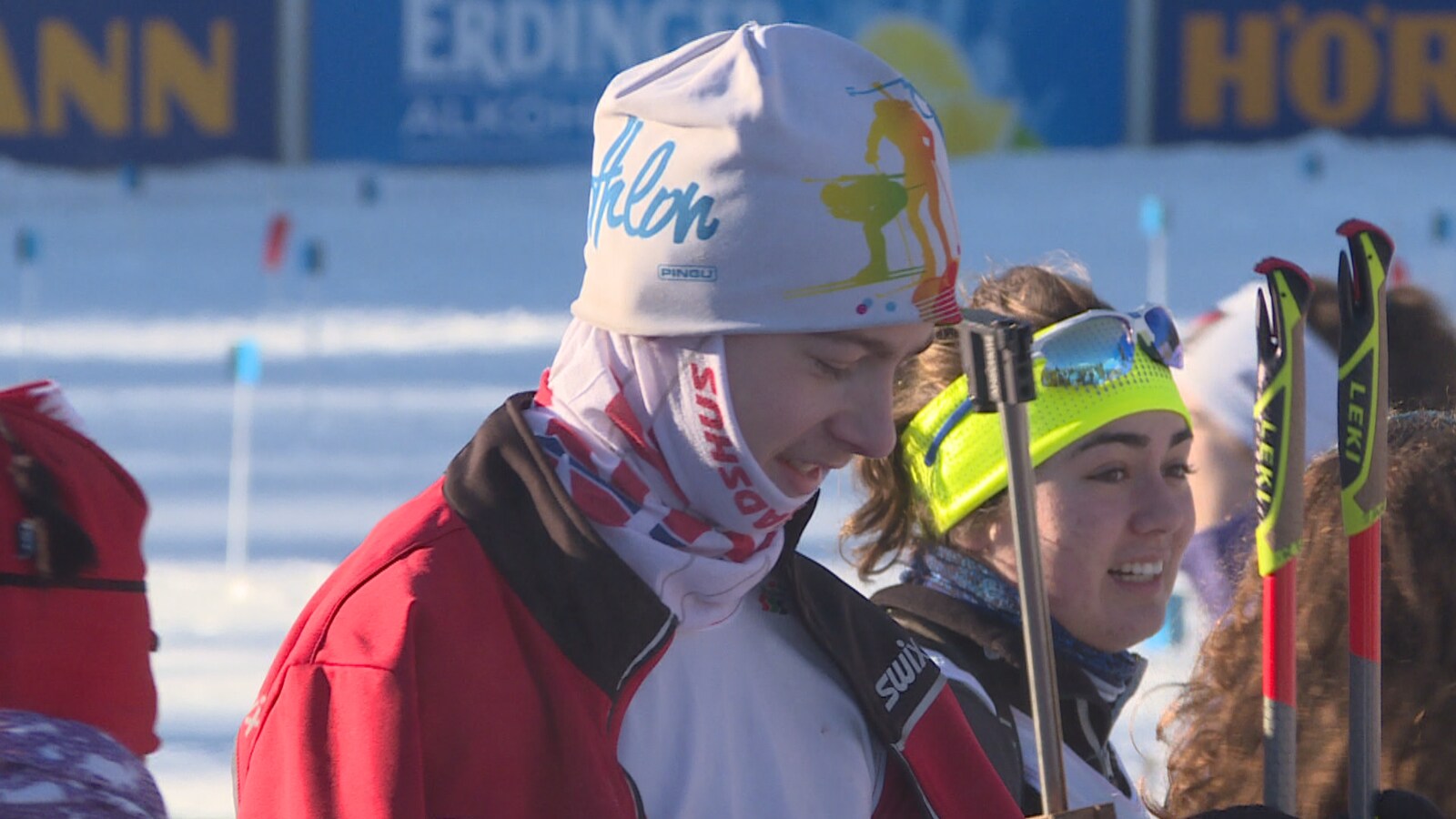 Des adolescents en jabits de ski sont debouts dehors, leurs bâtons de ski à la main. Timothé, avec une tuque blanche et un manteau rouge, est à l'avant-plan.