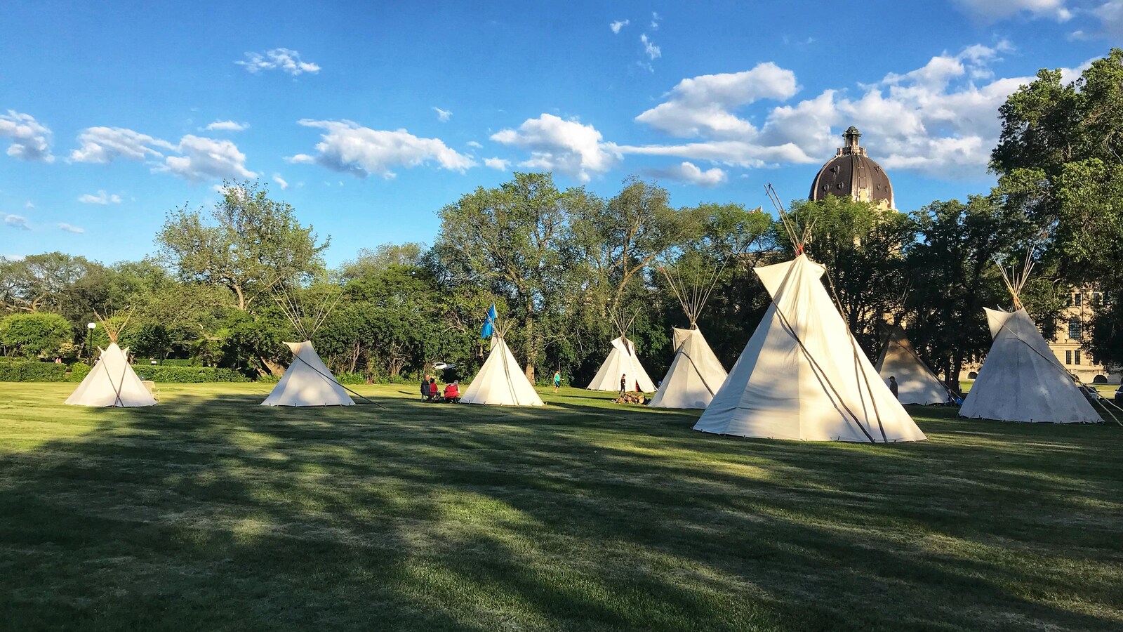 Sept tipis dansun parc, la coupole du palais législatif de Regina est en arrière plan.
