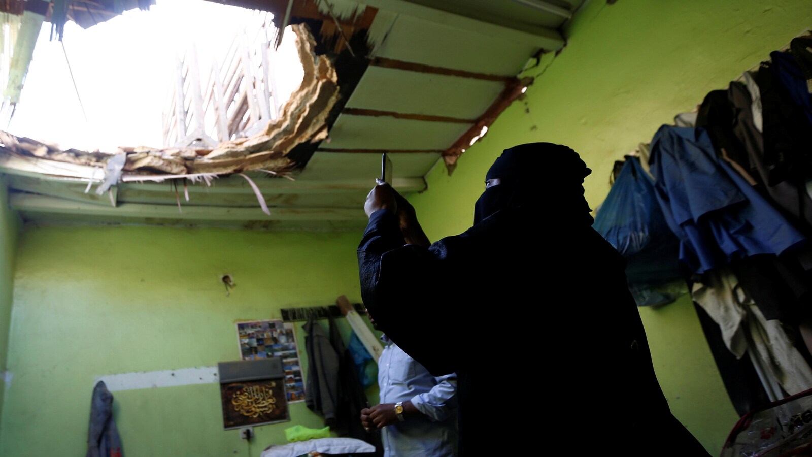 Une femme prend une photo d'un grand trou dans le toit d’une maison qui a été touchée par un missile.