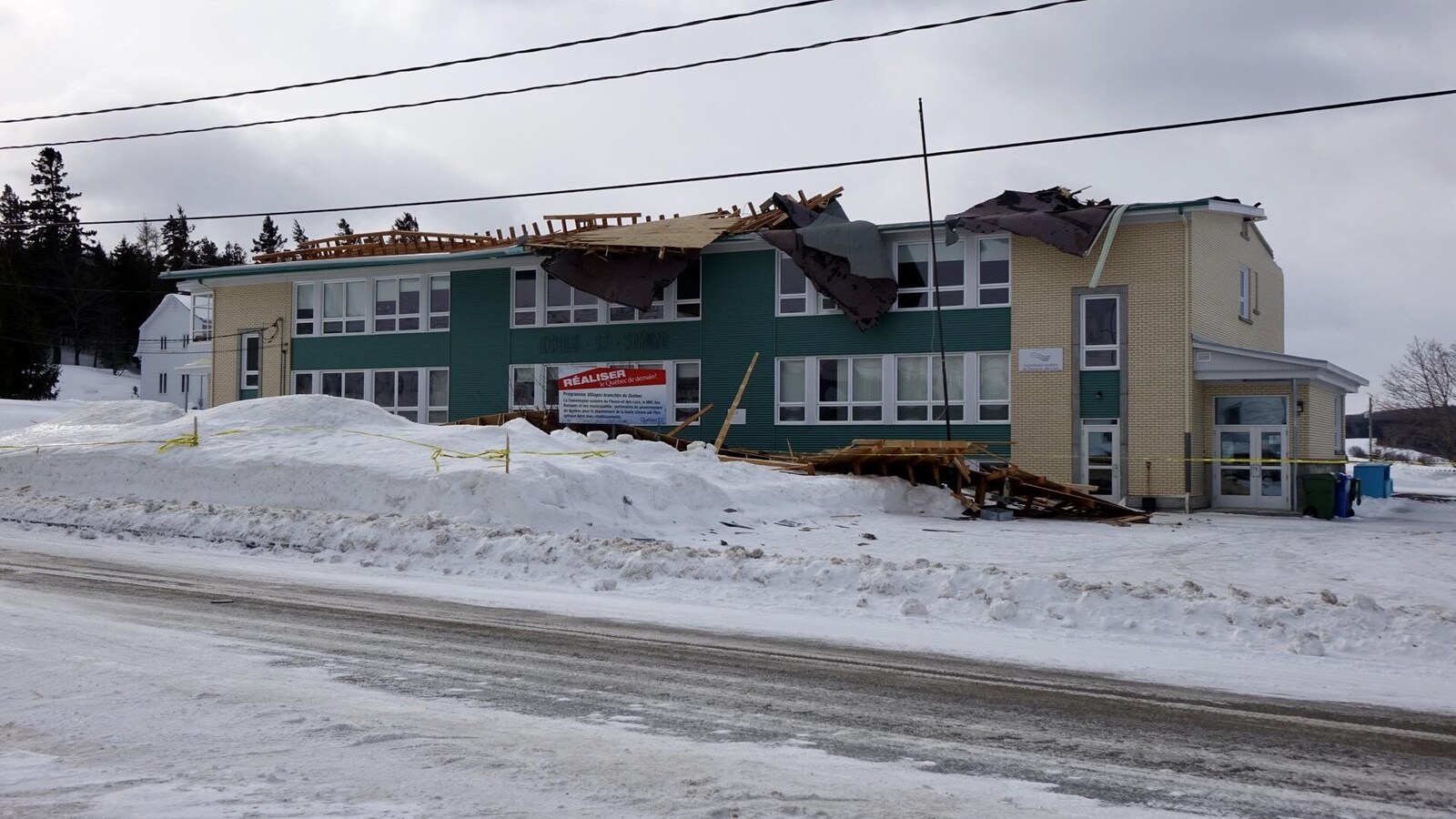 Un cordon de sécurité est installé autour d'un bâtiment à deux étages dont le toit est rempli de débris.
