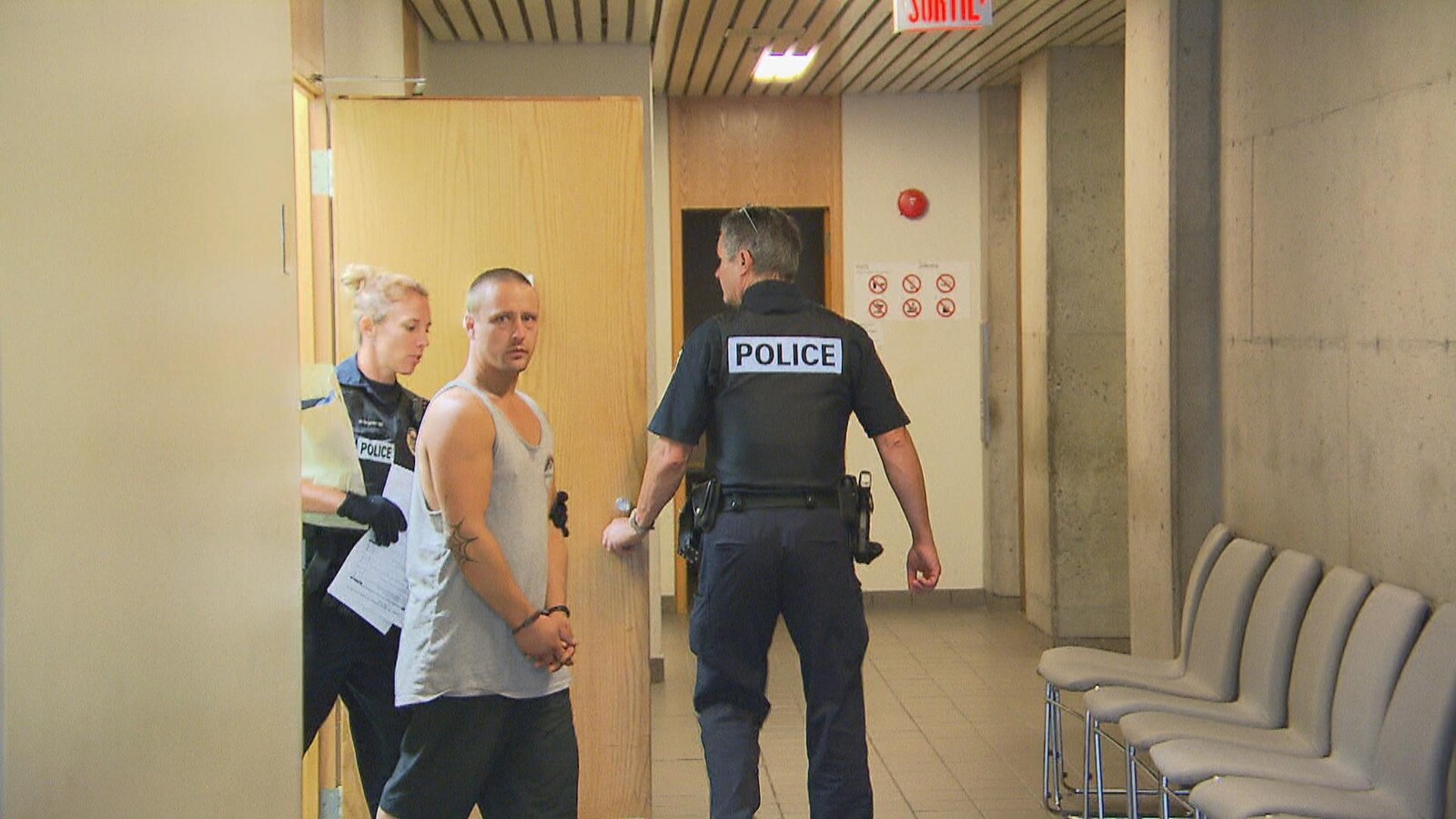 Un homme avec des menottes aux poignets est accompagné de deux policiers.