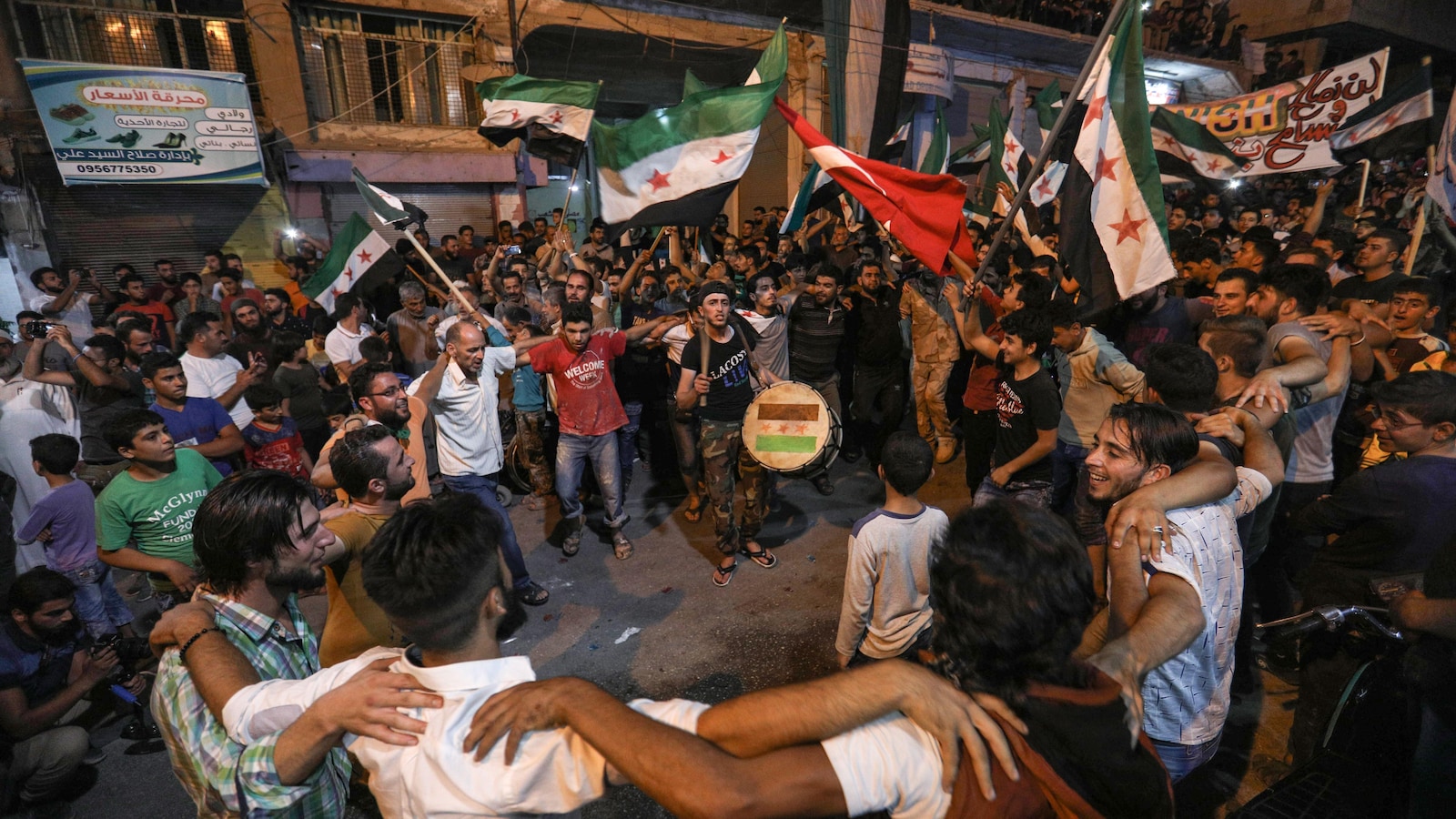 Des Syriens sont rassemblés dans la rue et dansent en agitant des drapeaux.