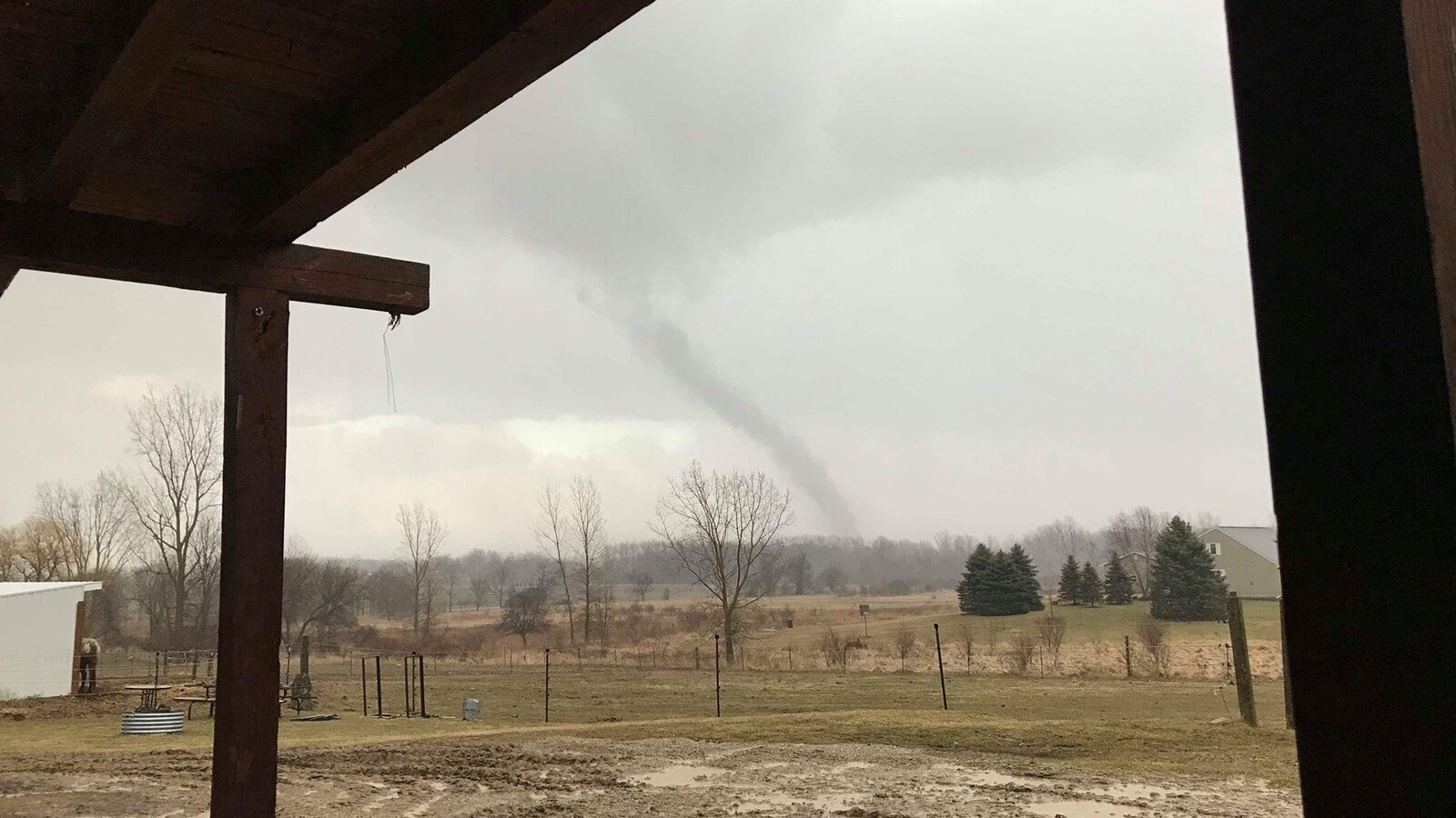 On voit un champ, une écurie, au loin à l'horizon se dessine une tornade, le ciel est gris.