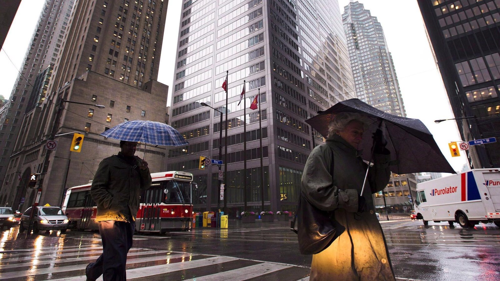 Deux passants traversent une grande artère en s'abritant sous des parapluies dans le quartier financier de Toronto.