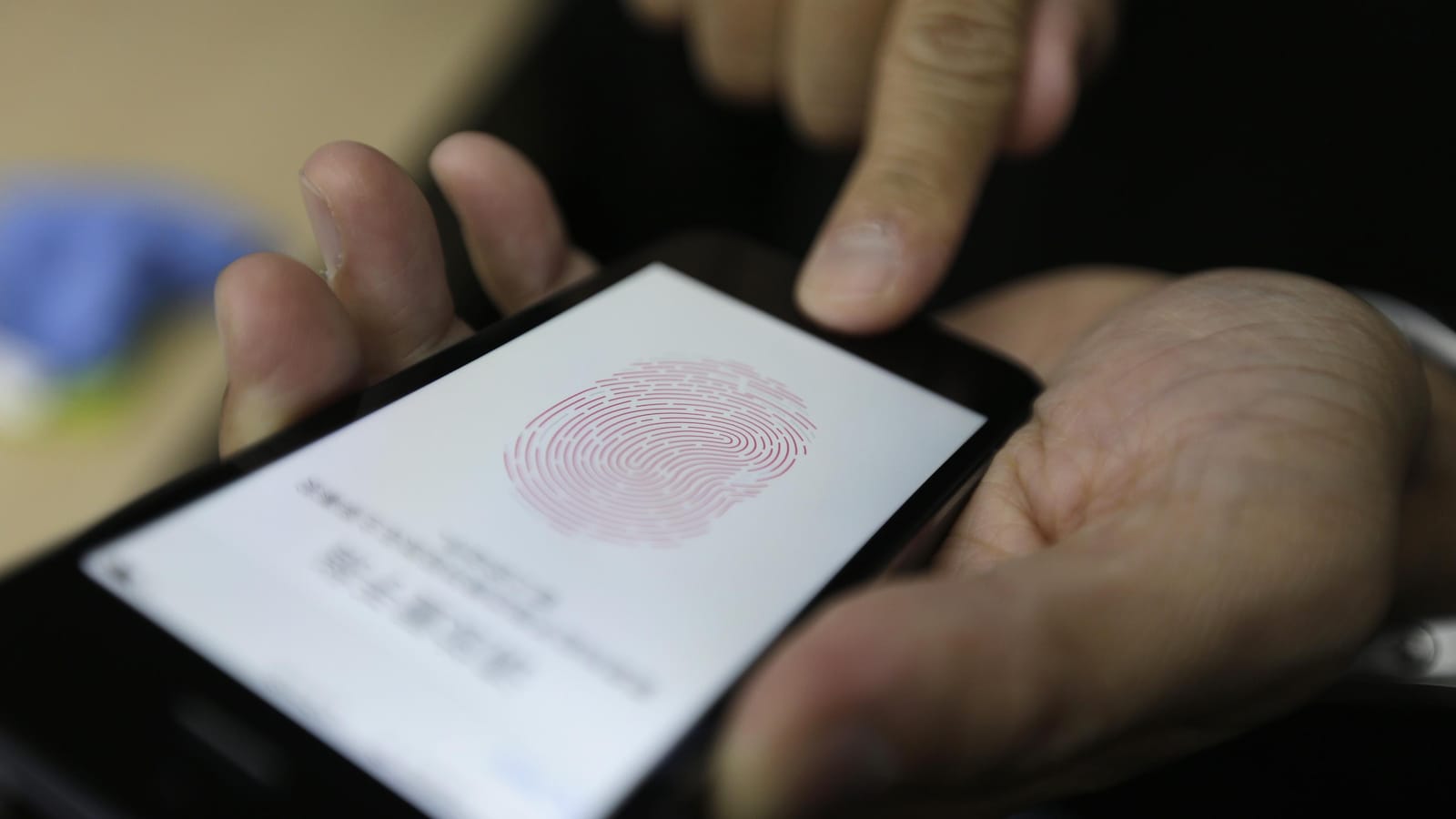 Une photo montrant les mains d'une personne qui tient un iPhone sur l'écran duquel est affichée une empreinte digitale. La personne appuie sur le lecteur d'empreintes digitales avec son index droit.