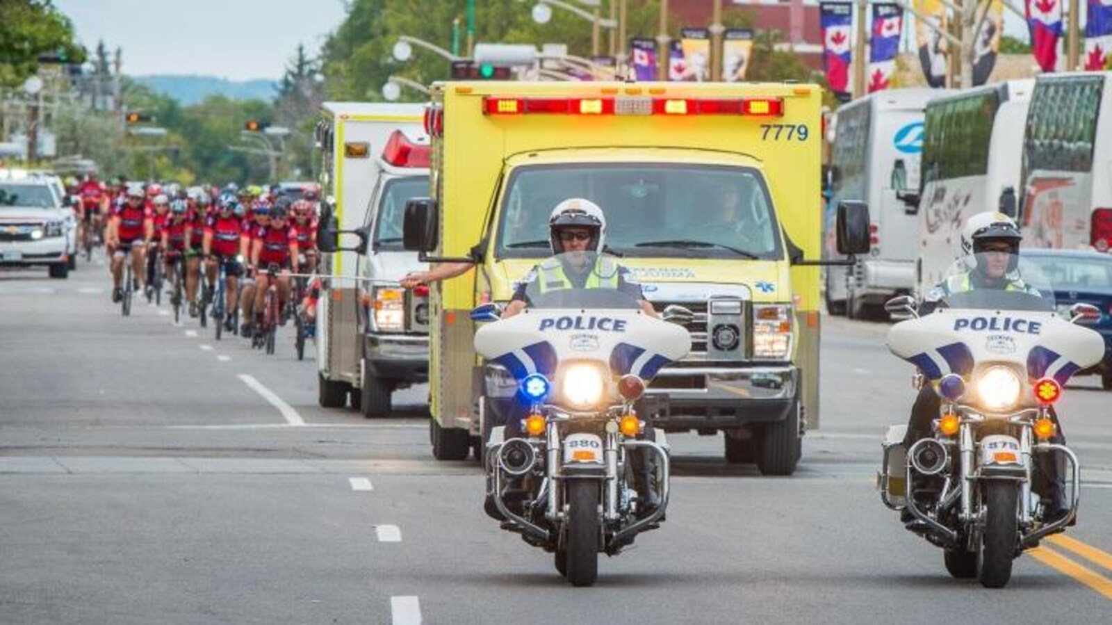 Deux motos de police suivies de deux ambulances et d'un peloton de cyclistes.