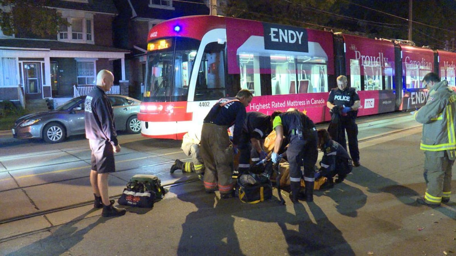 Photo d'ambulanciers accroupis près d'une victime au sol, un tramway en arrière-plan