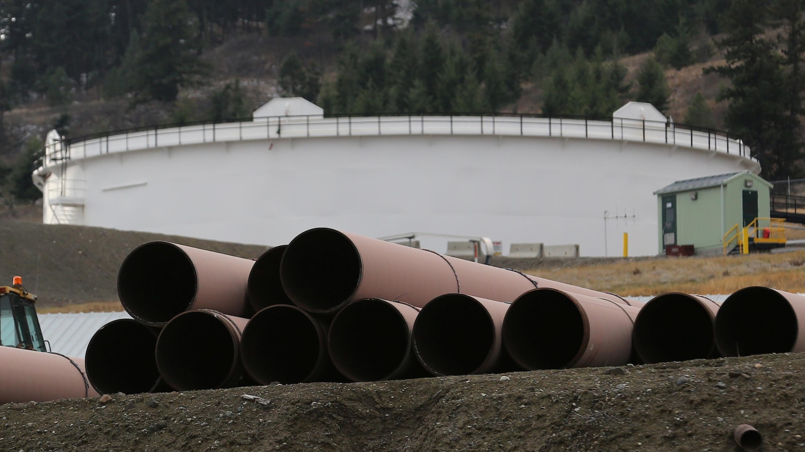 Des tuyaux devant servir à transporter du pétrole avec, en arrière-plan, un réservoir dans la région de Kamloops, en Colombie-Britannique.